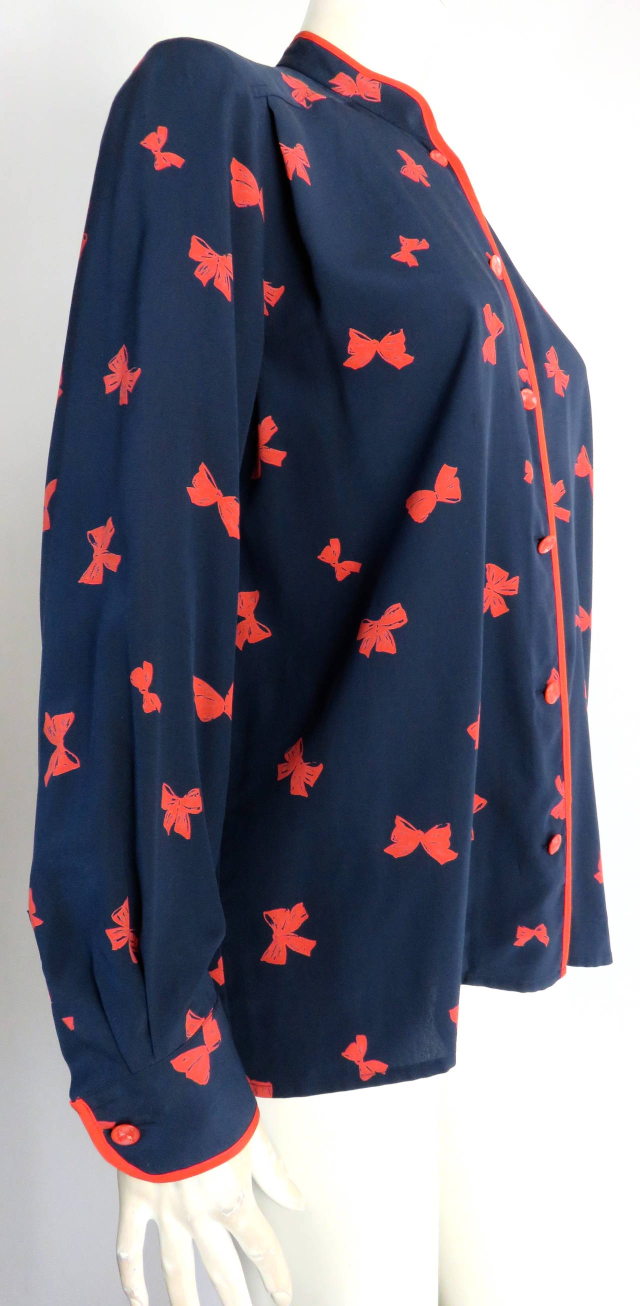 Adorable, 1980's CELINE PARIS Silk bow-tie print blouse shirt in dark navy blue ground and red artwork.

Mandarin collar shape with logo engraved, pearlized, red button closures at front placket.

Solid red silk binding fabric along top edge of