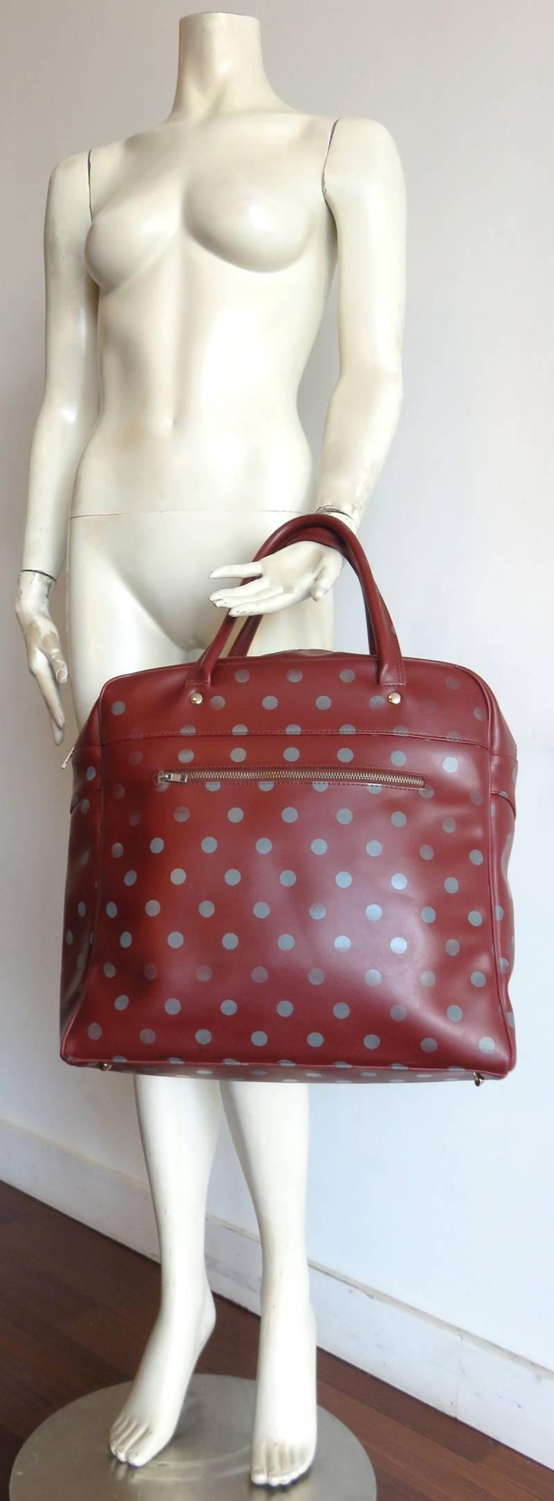 COMME DES GARCONS Polka dot travel bag.

Dark red ground with gray polka-dots.

Metal zip front pocket on front exterior.

Metal zip at top opening with zipper pocket at interior with second stash pocket as well.

Fully lined in black