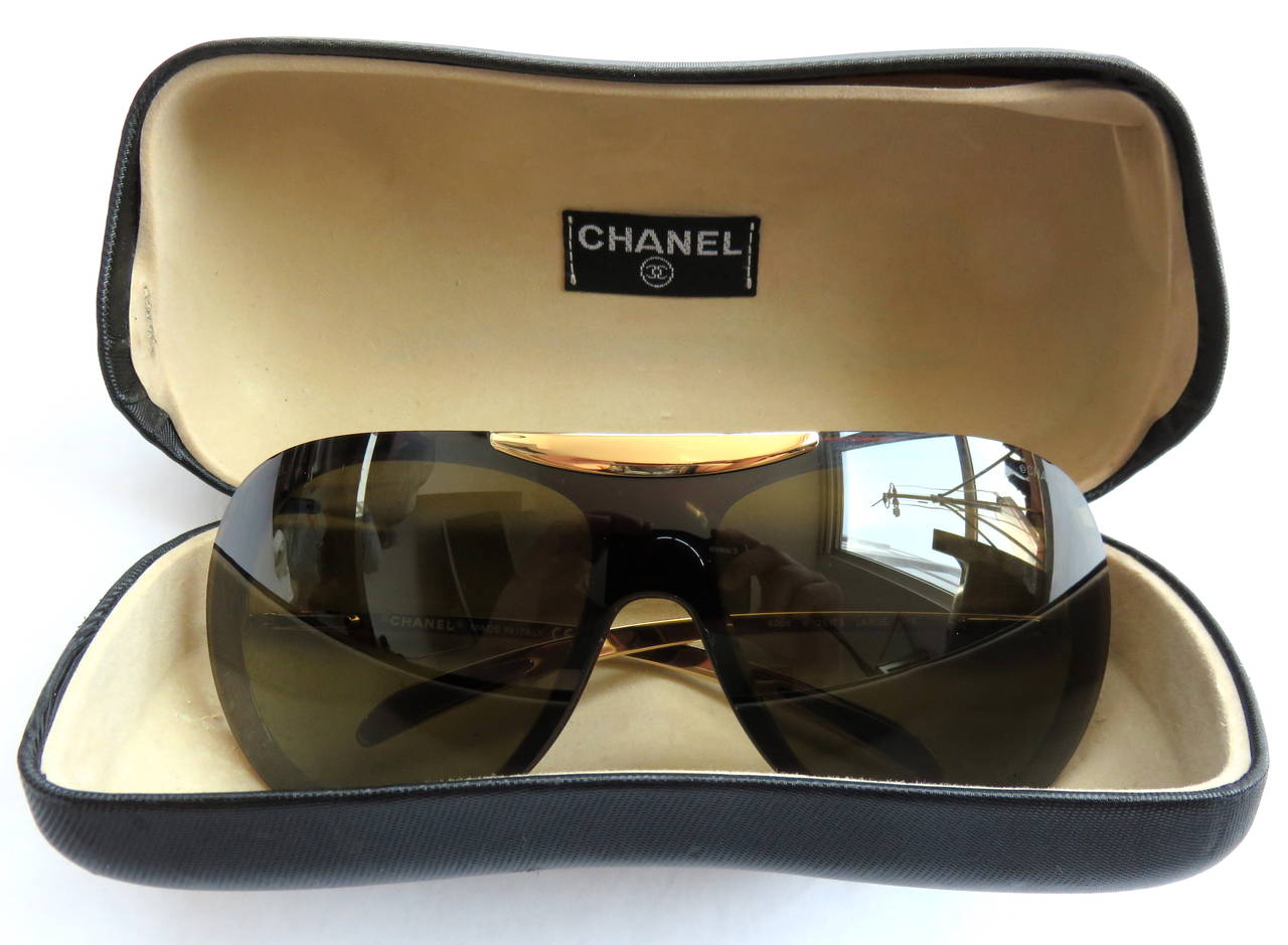 Worn once, excellent condition, CHANEL PARIS, Shield-style sunglasses with logo engraved, gold-finished metal trim details at top, and sides.

Brown tinted lens with no damages, or scratches. 

Includes the original, hard-cover carry