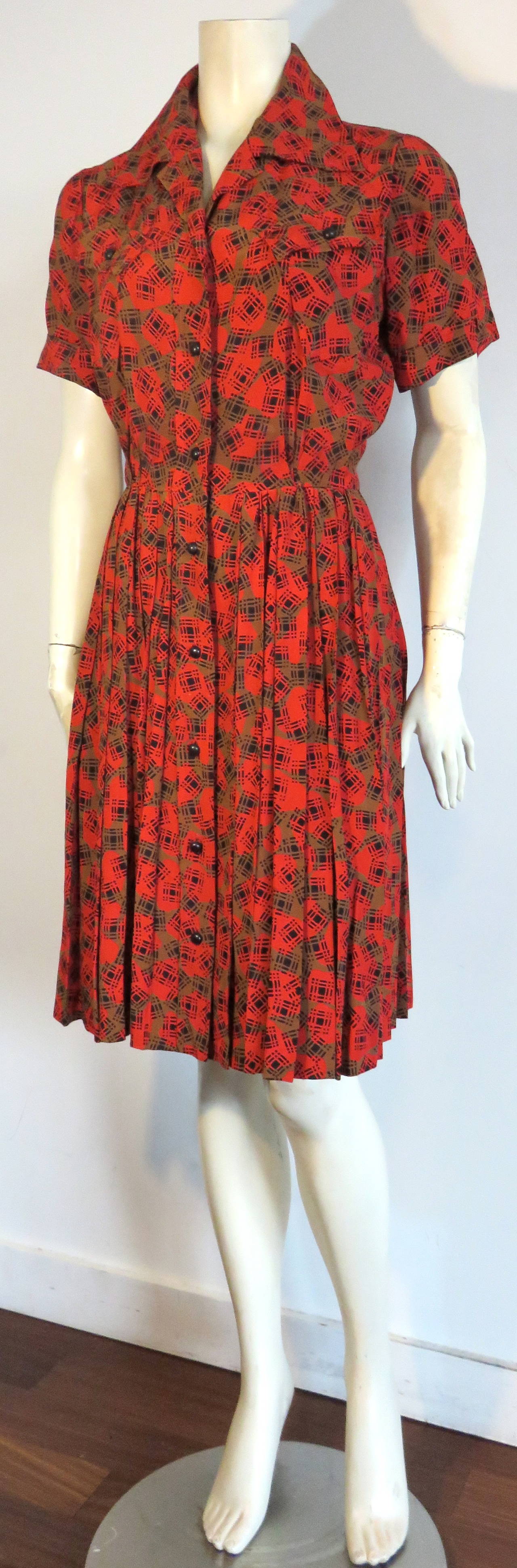 1970's YVES SAINT LAURENTSilk button down day dress.

Red & olive ground print with black grid/check over print motif.

Twin chest pockets.

Pleated bottom skirt with concealed hook and eye closure at the waist opening.

Made in France, as