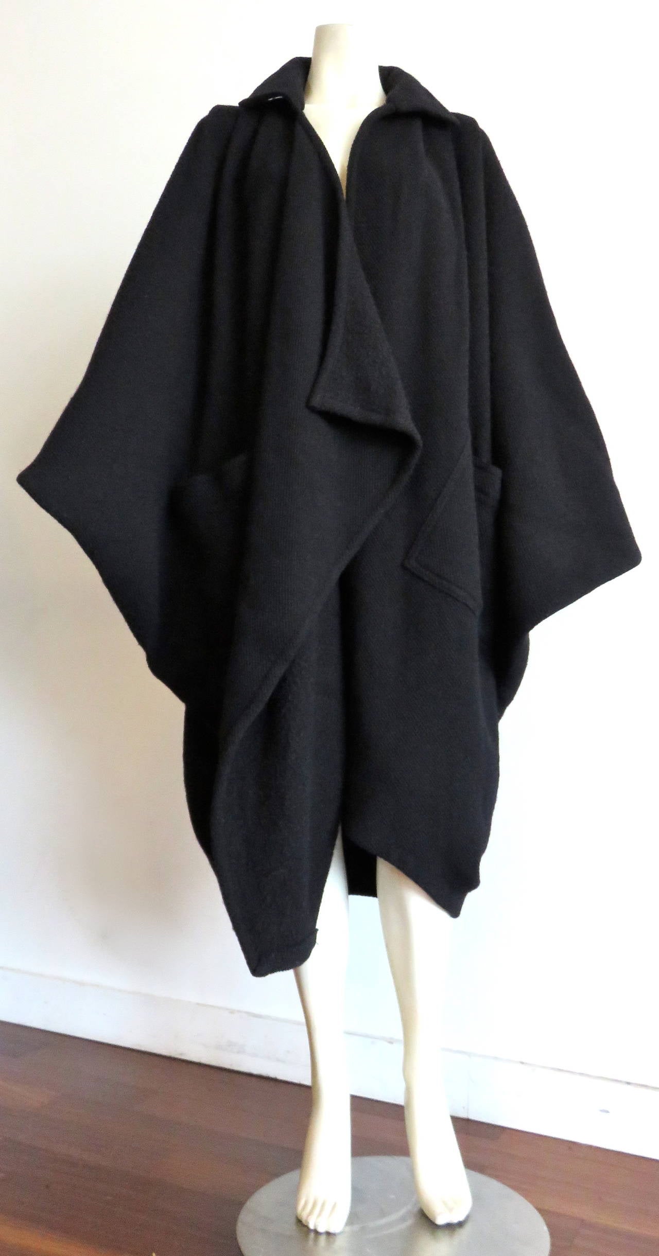 Fabulous, 1976, ISSEY MIYAKE, black, oversized batwing/cocoon coat in wool twill, woven fabric.

Open front design with twin patch pockets at the waist level.

Voluminous, diamond-shape silhouette with pleated construction at the front shoulders