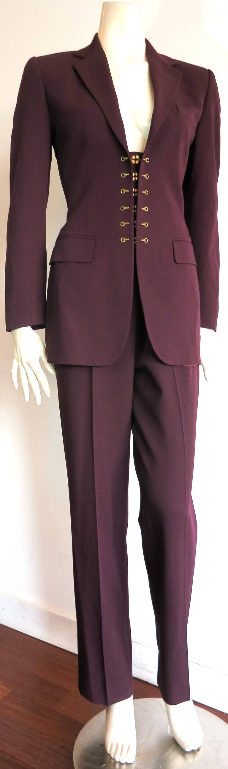 JEAN-PAUL GAULTIER PARIS Brass hook pant suit in dark wine tone, virgin wool.

The jacket features double headed, brass hook closures at the front with brass eyelets at both sides.

Twin flap pockets at waist.

Concealed zipper at left side