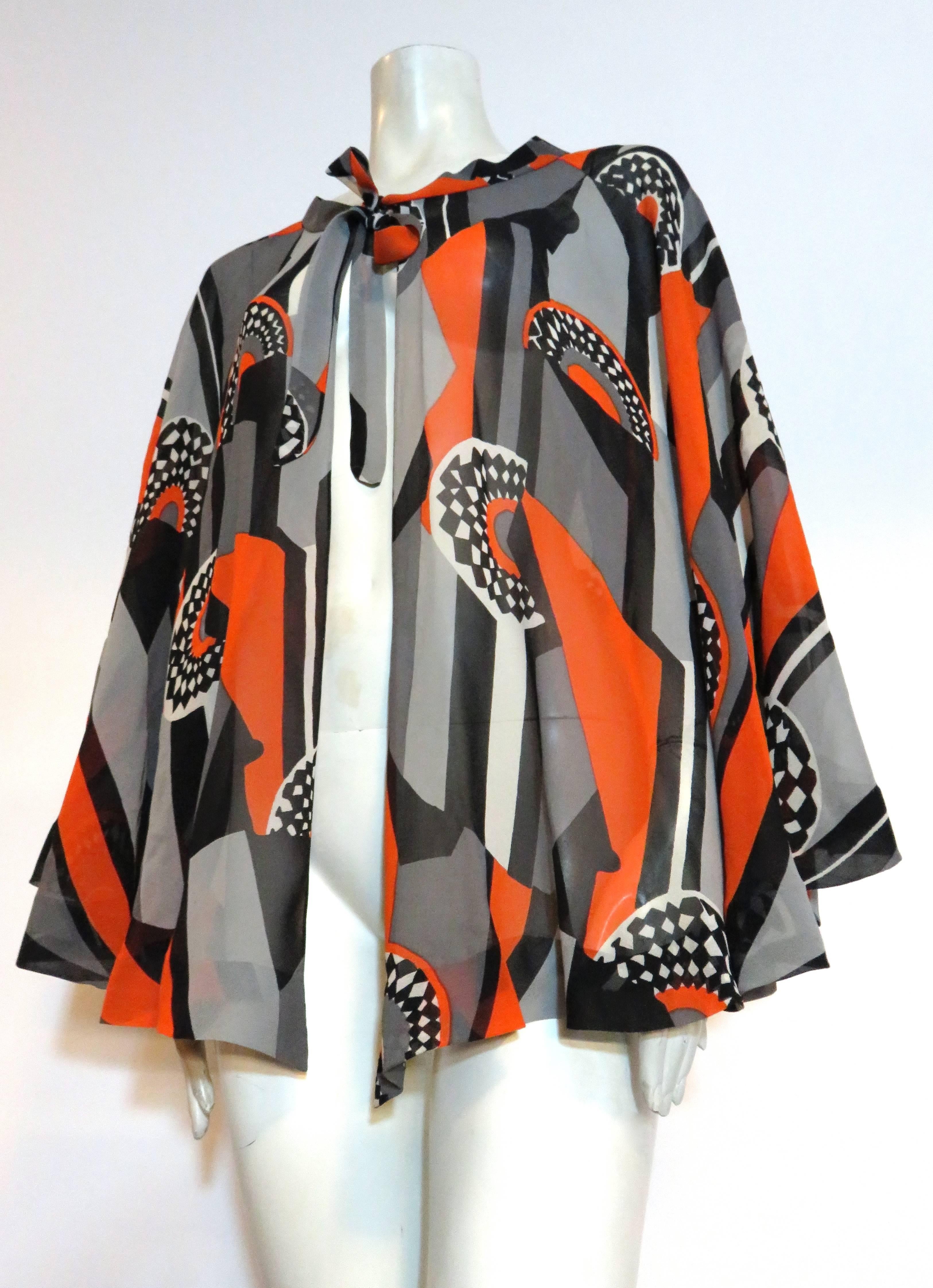 Excellent condition, 1970's LA MENDOLA Deco printed silk cape.

Semi-sheer, silk chiffon fabrication with wonderful, art-deco inspired artwork print in tangerine, black, and gray.

Tied neck for an adjustable fit.  The cape can really