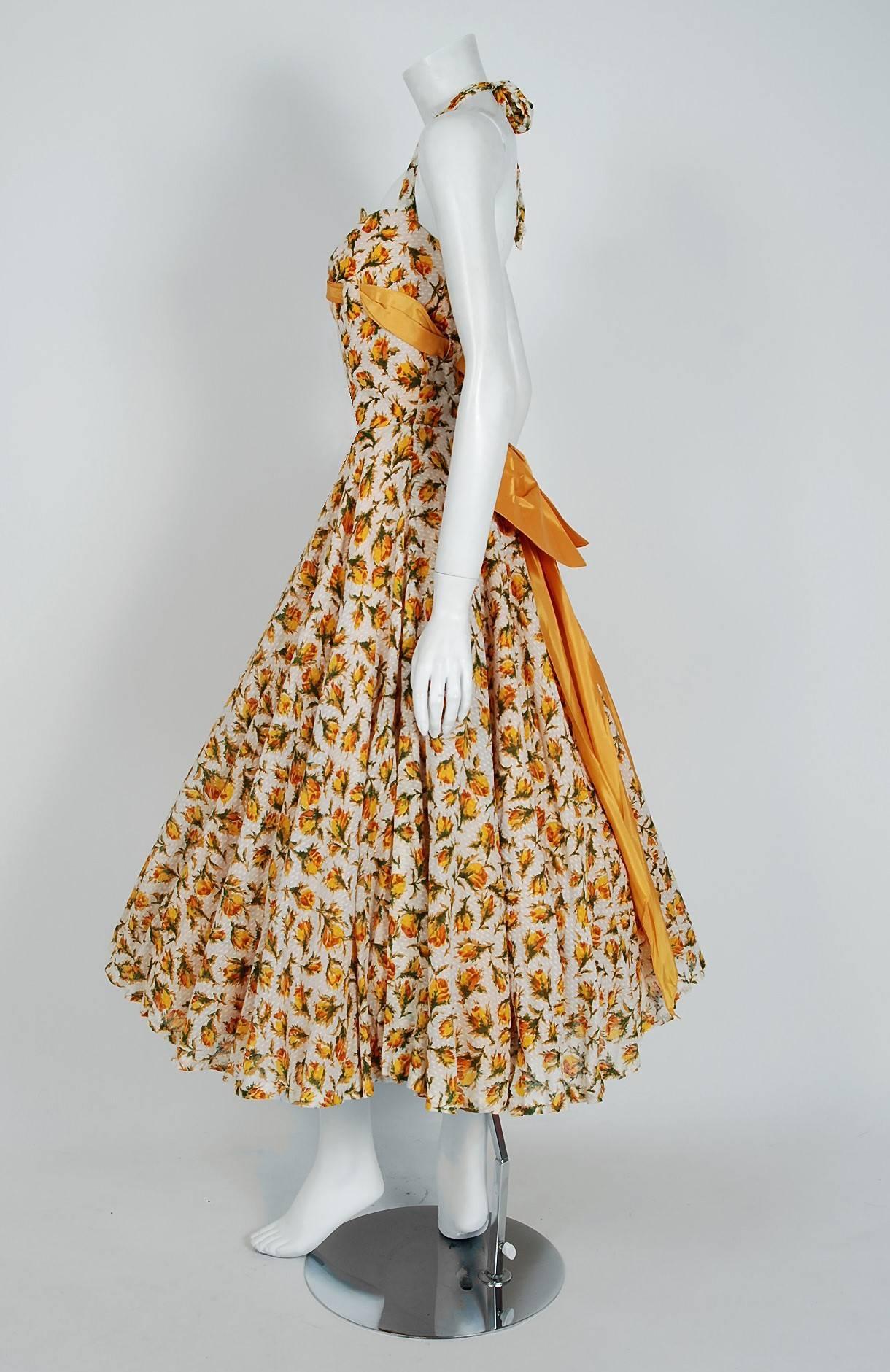 An amazing and highly stylized 1950's sundress by Lilli Diamond. With its gorgeous marigold-yellow roses floral print and flawless styling, this garment has the casual elegance the 1950's were known for. The low-cut scalloped plunge halter bodice is