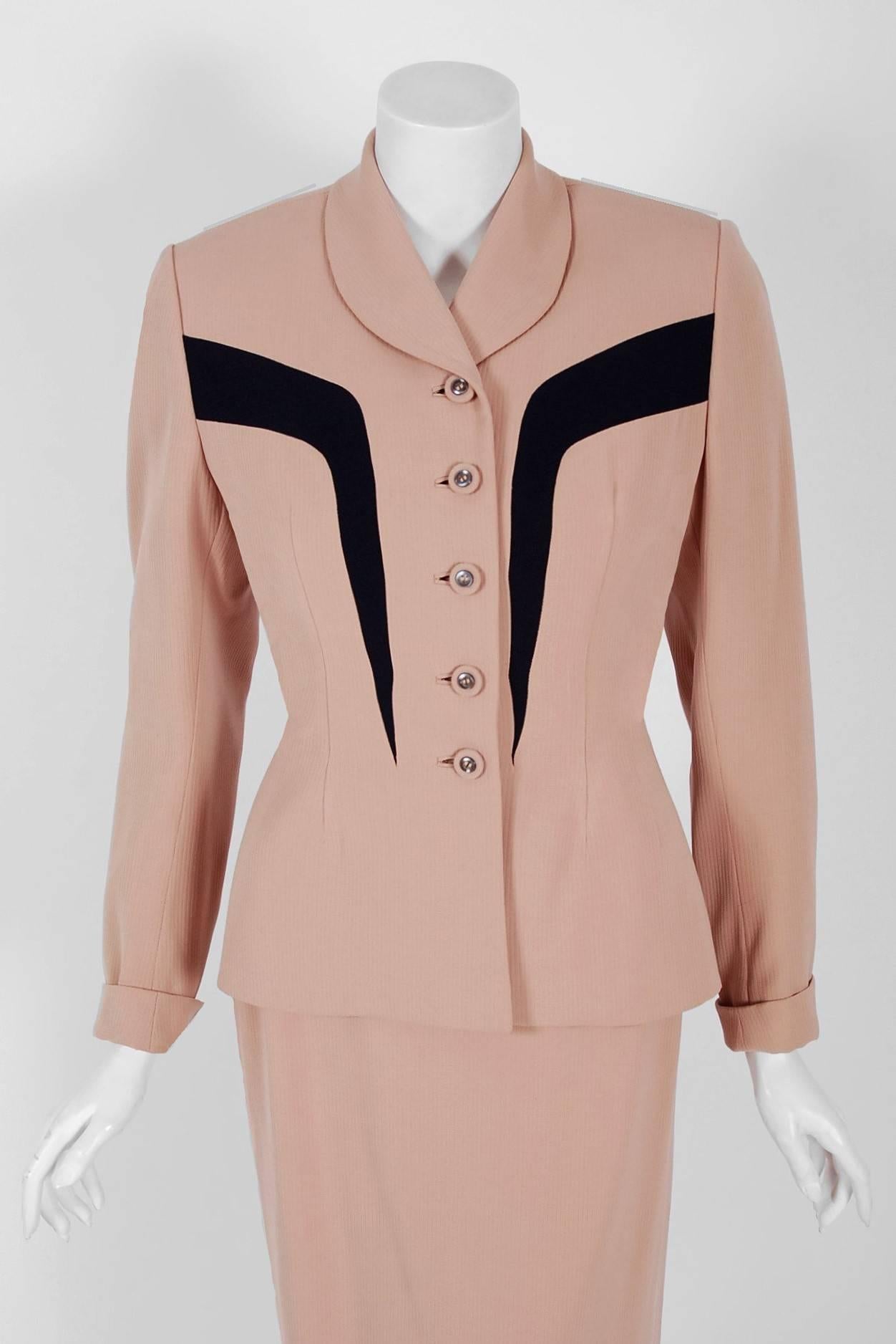 This stunning 1940's Carlane Originals two-piece ensemble is fashioned in blush pink and navy Forstmann virgin-wool. The fabric itself is a masterpiece; vertical woven wool that seems to have an almost 3-dimensional feel without being stiff or