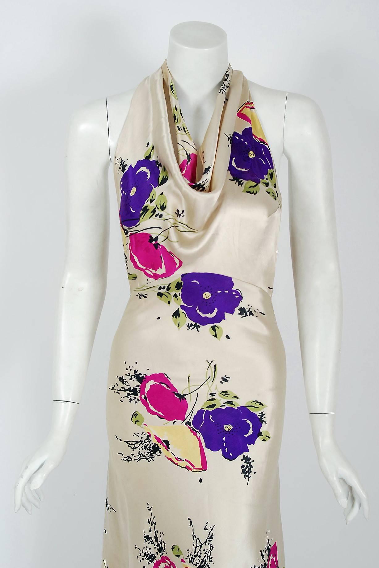 A rare luxurious floral-garden print silk satin gown from the "Old Hollywood" era of glamour. The bodice is an ultra chic cowl-neck with stylized cut-out twist backside. The waist is nipped with a tailored back belt. The lower skirt is