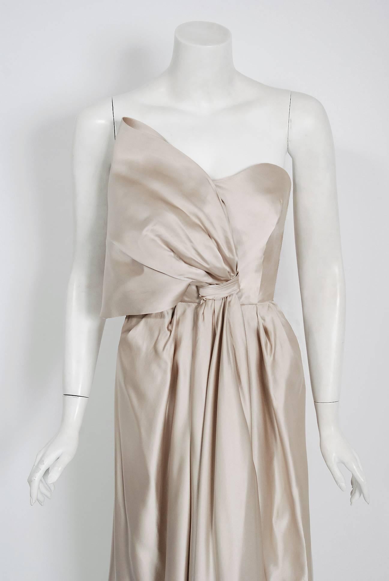 A breathtaking Saks Fifth Avenue champange silver shimmer silk-satin gown from the Old Hollywood era of glamour. The bodice has a unique sculpted asymmetric draped bow with seductive boned strapless! I adore the hourglass nipped waist