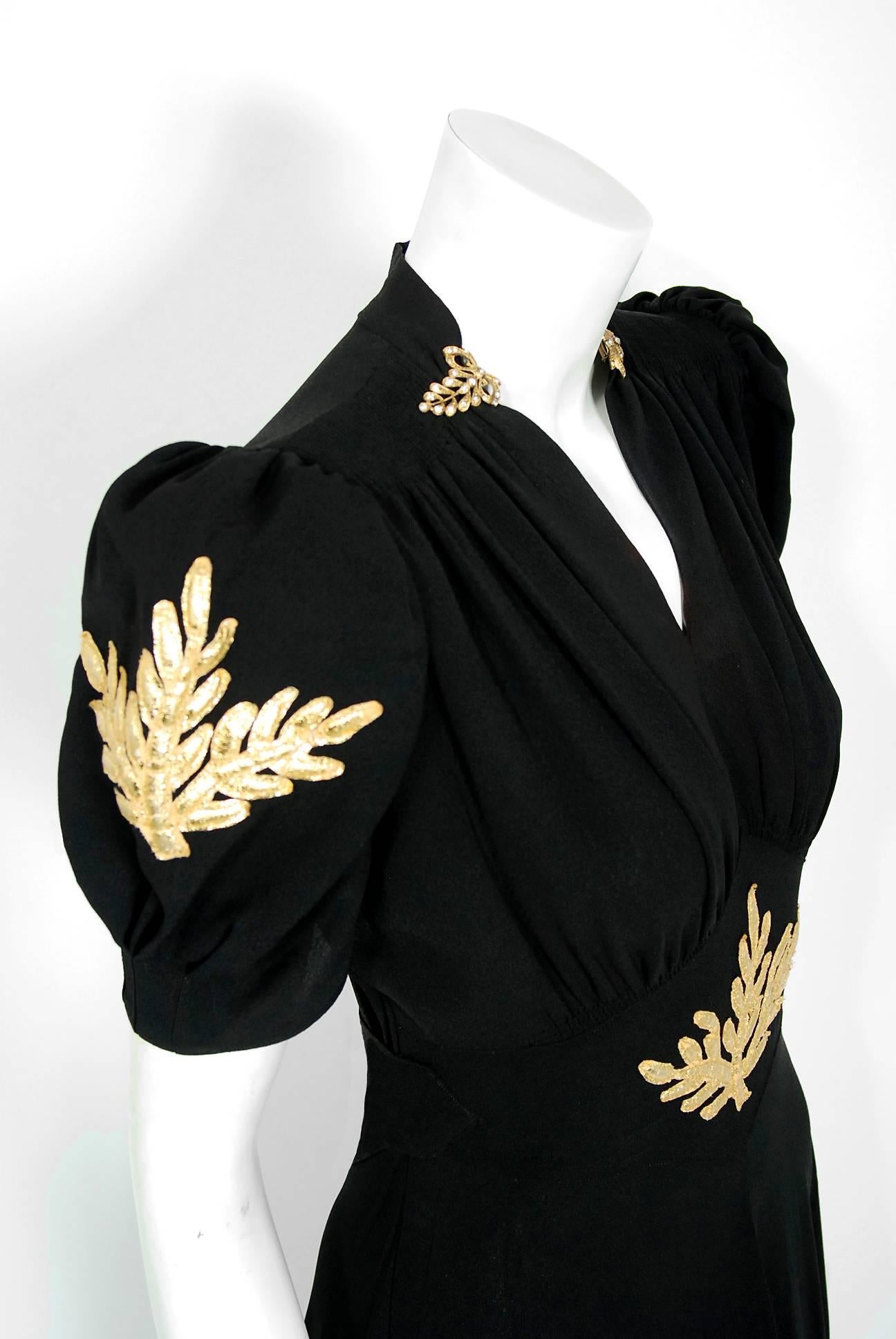 A gorgeous jet-black rayon crepe gown from Old Hollywood era of glamour. The bodice is a seductive rhinestone-paste trimmed low plunge ruched bias-cut with dramatic puff sleeves. I love the metallic-gold lame leaf motif applique work which really