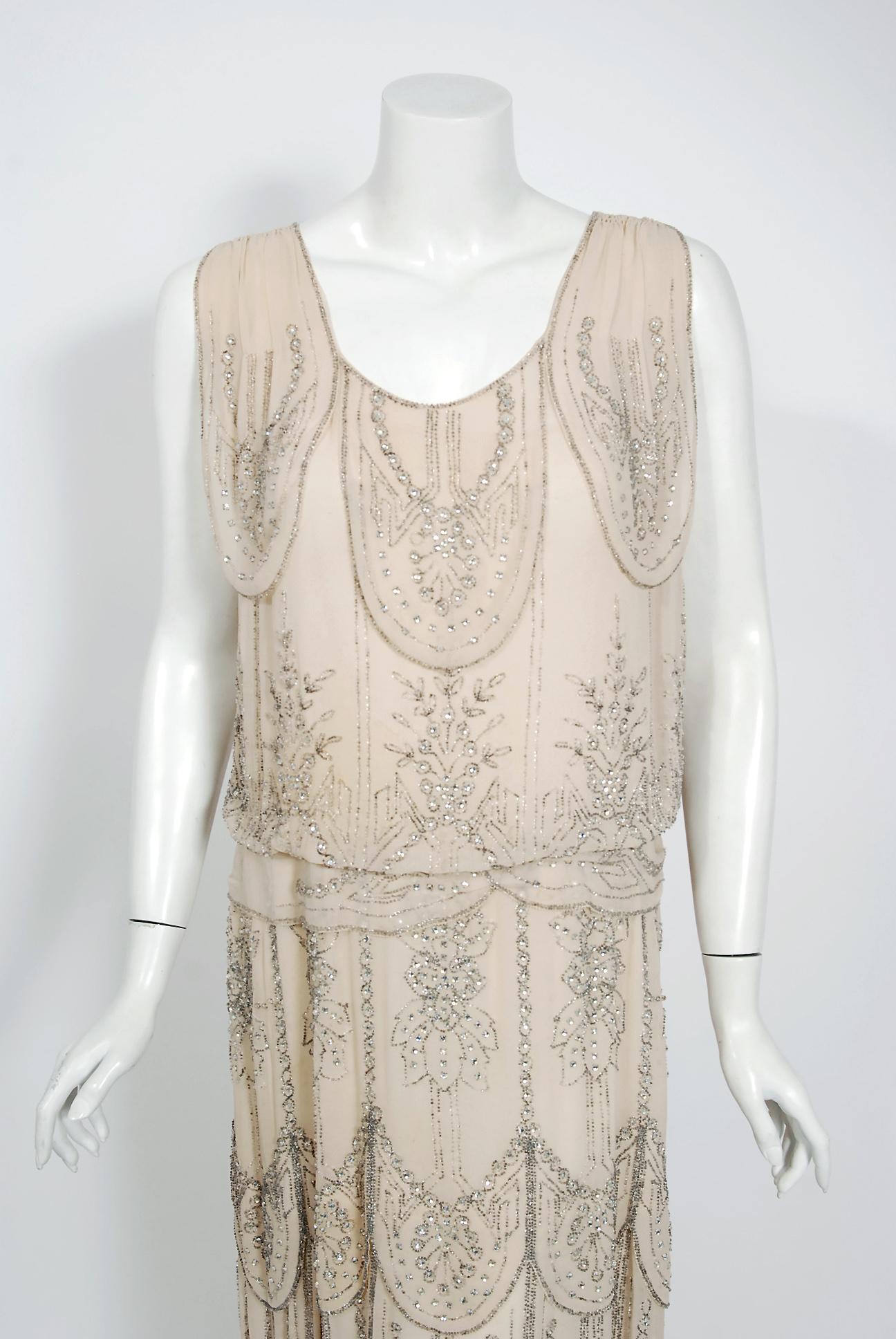 Undiminished by time, this early 1930's ivory-creme couture gown still casts its magical spell. This exceptional French beauty is fashioned in triple layered high-quality silk chiffon. It is then lavishly embellished with prong-set rhinestones and