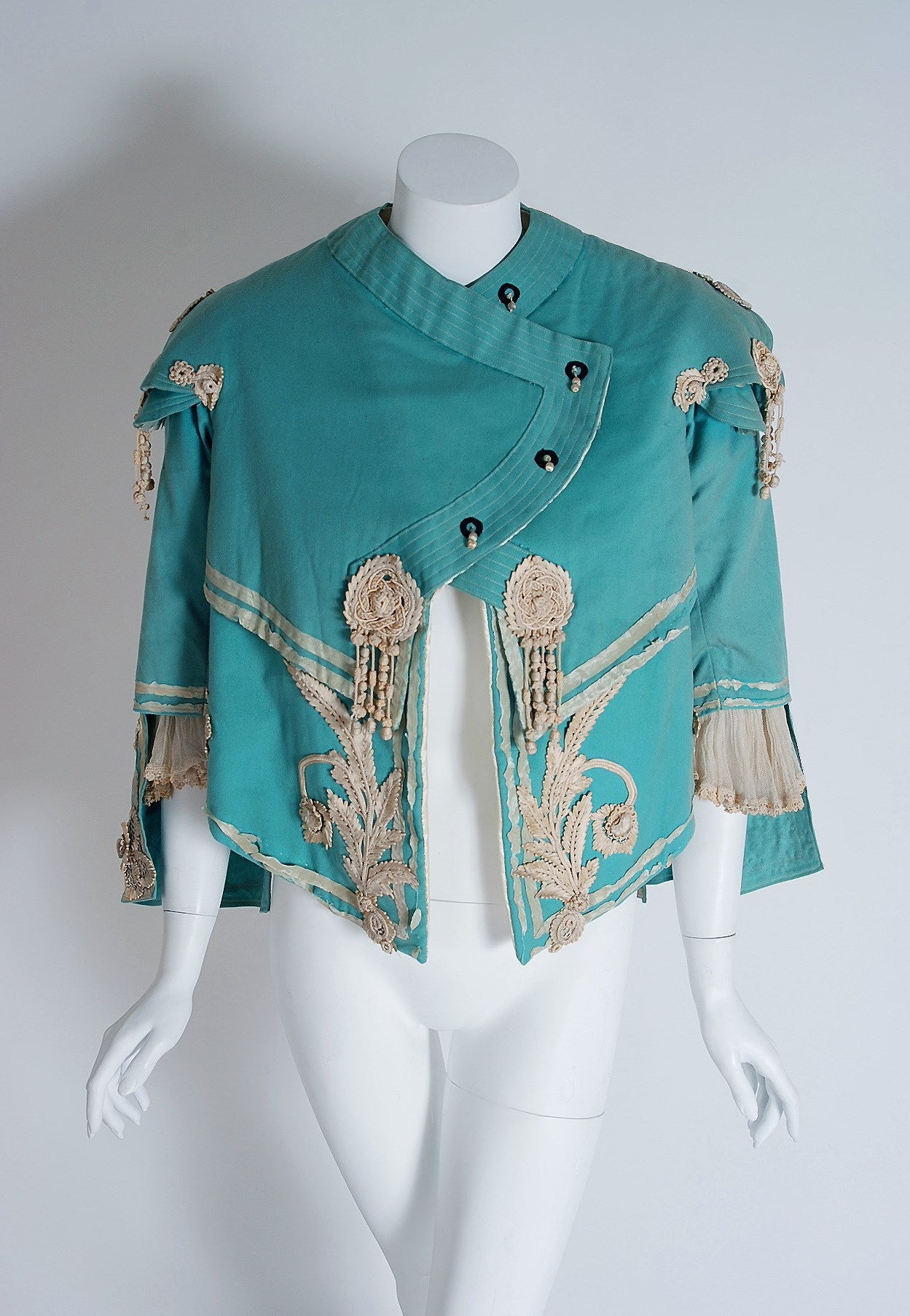 This breathtaking custom-made Victorian cropped jacket dates back to the 1890's. It is lavishly embellished with the finest ivory lace floral motifs and fringe applique. I adore the winged bell-sleeves and asymmetric front closure. The layered