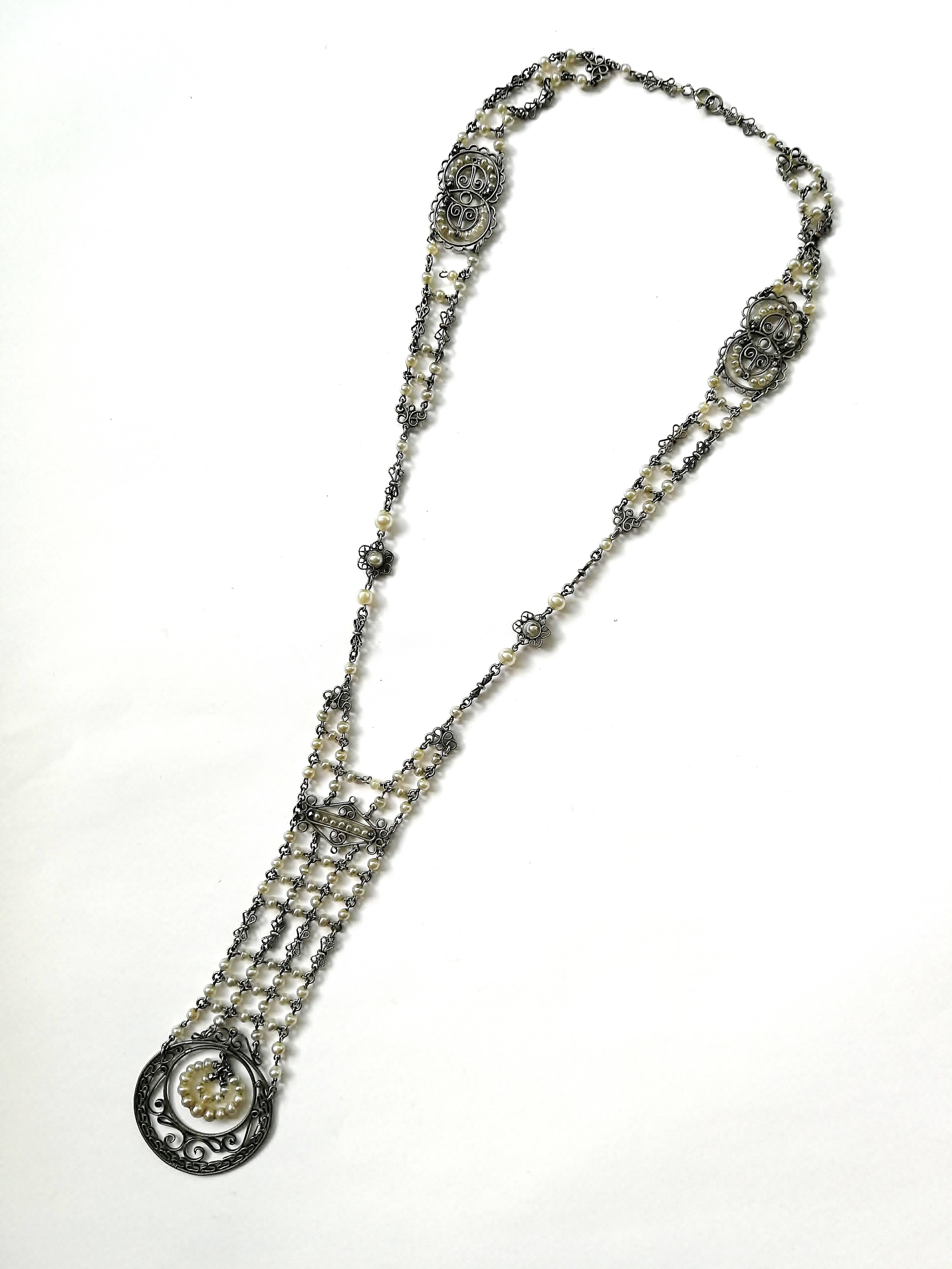 This beautifully delicate and fine necklace appears like lace or similar, all articulated, made from fine silvered metal links and filigree floral motifs, and small glass pearls into an very flattering shape and design. 
Made in France in the 1920s,