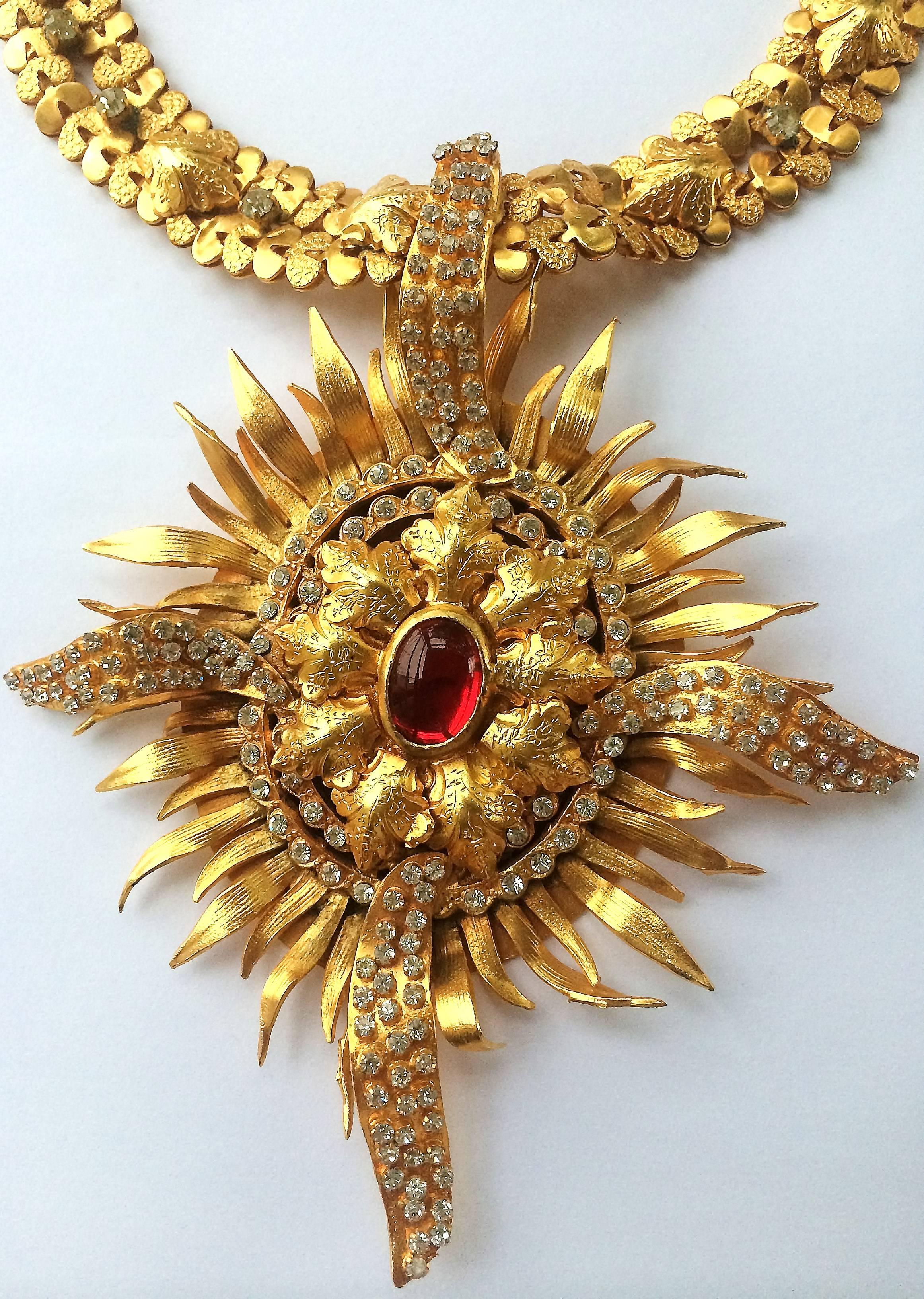 This is a rare, handmade French necklace in gilded worked metal with a sculptural twist to the 'flames'. The linked collar of alternating hammered and embossed/plain links highlighted with a gilded leaf motif and white paste. 
The pendant has a