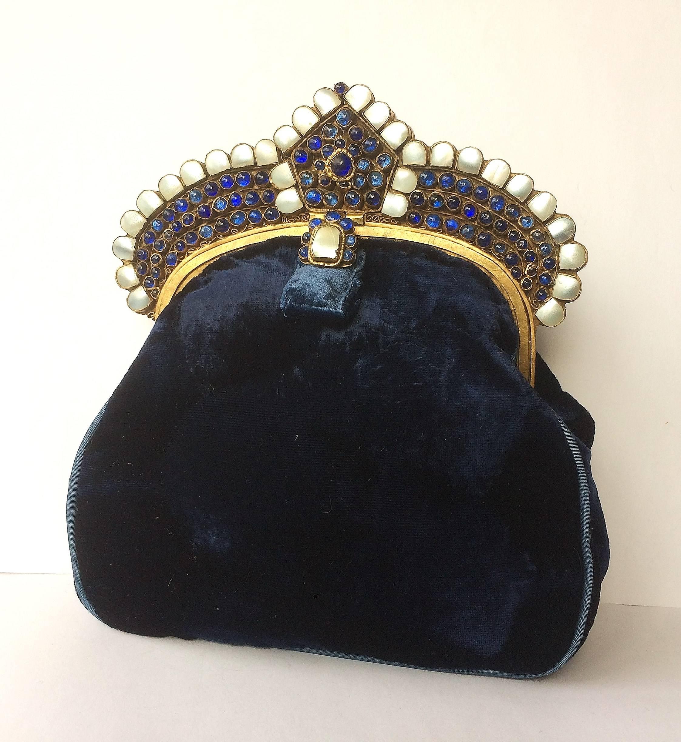 A sumptuous, rich, dark blue clutch bag from the 1920s, in a distinctive Moghul style, made from Royal blue silk velvet, most likely French in origin.
The frame is made from base metal/brass, set with sapphire 'poured glass' cabuchons and mother of