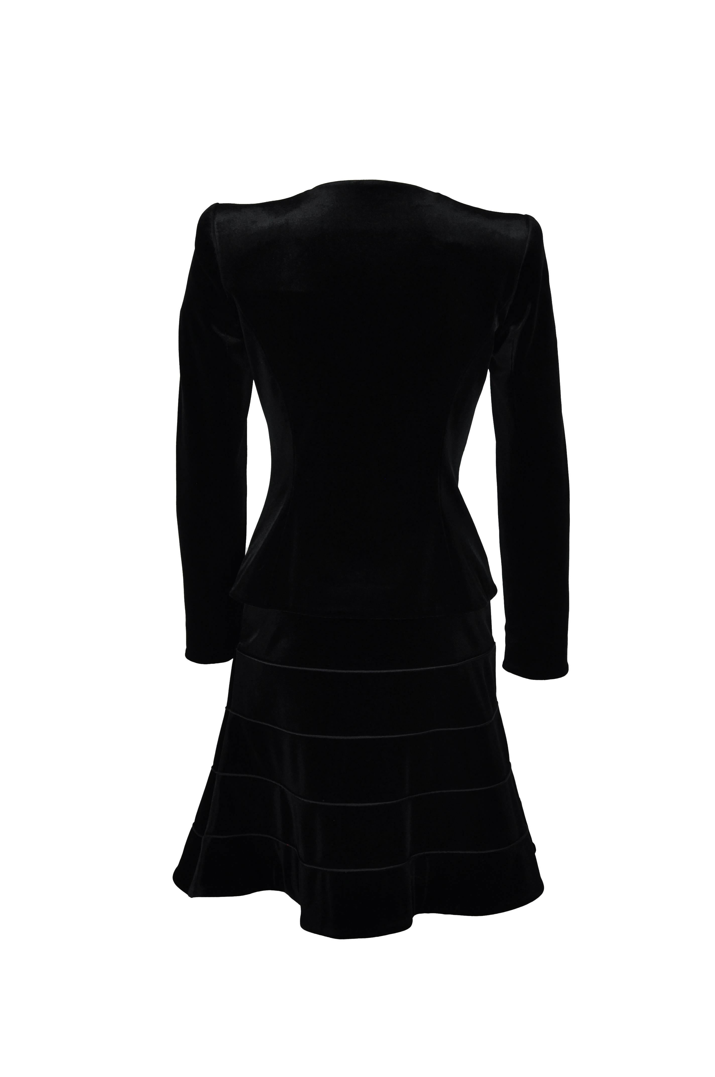 A timeless and elegant fitted black stretchy velvet jacket with A-line panel skirt.
The collarless jacket features a large black satin bow at front with two snaps and loop fastenings. The skirt has zip at side. Fully lined
 