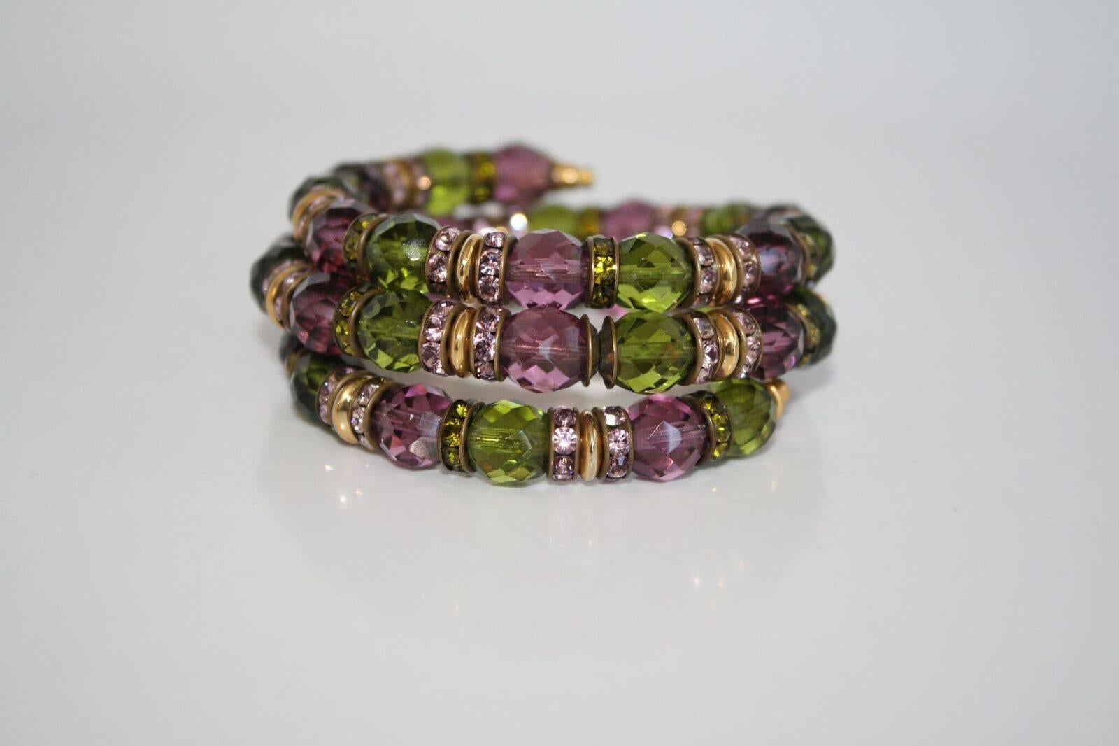 Green and purple faceted glass beads surrounded by Swarovski crystal and gold beads in this memory wire bracelet from Francoise Montague. 