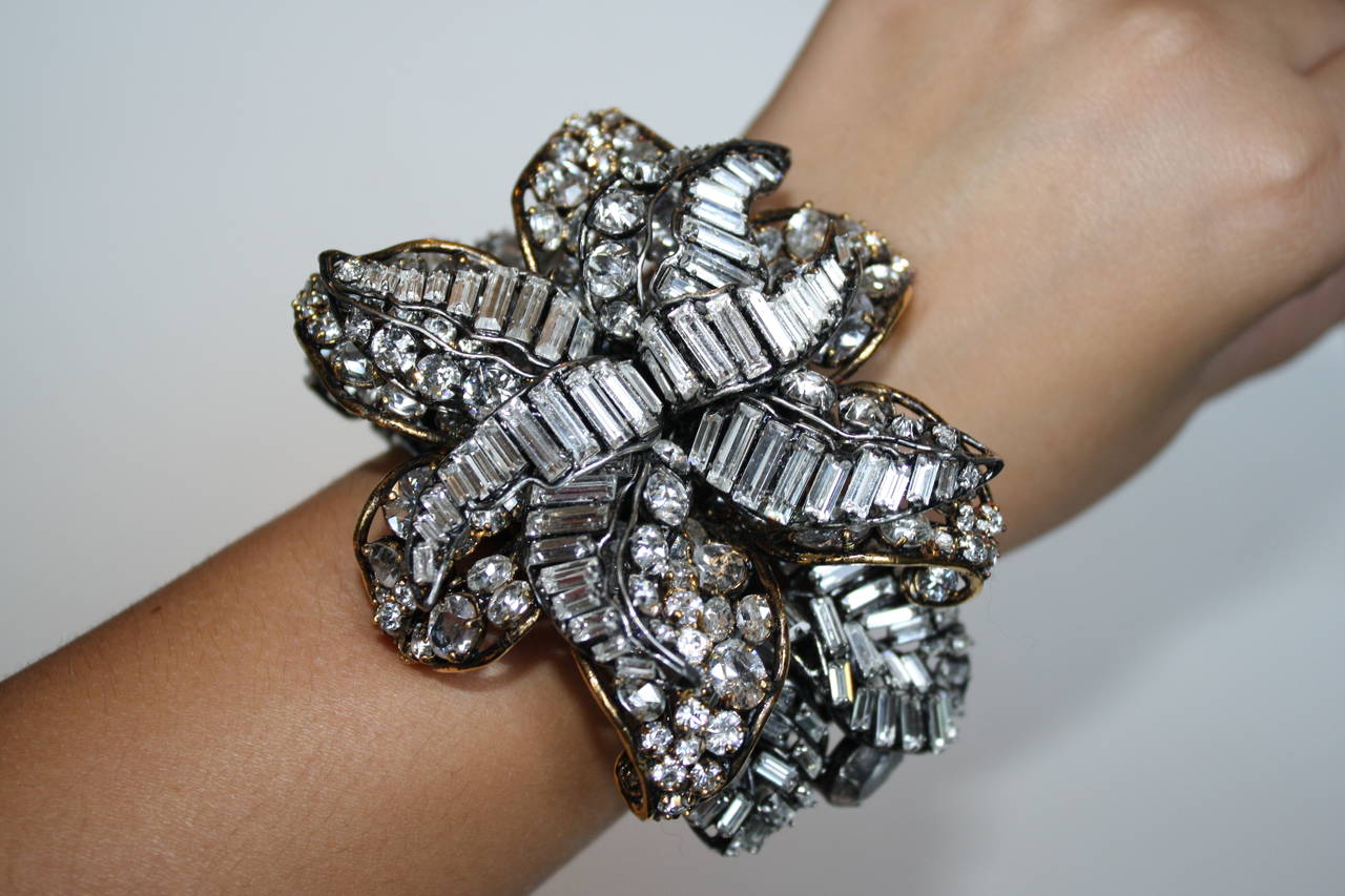 An extraordinary oversized floral motif cuff from Iradj Moini made with foil backed Swarovski crystals and cubic zirconium. The top flower comes off and can be worn separately as a brooch. Cuff is hinged, allowing for easy on and off. 

2.25"