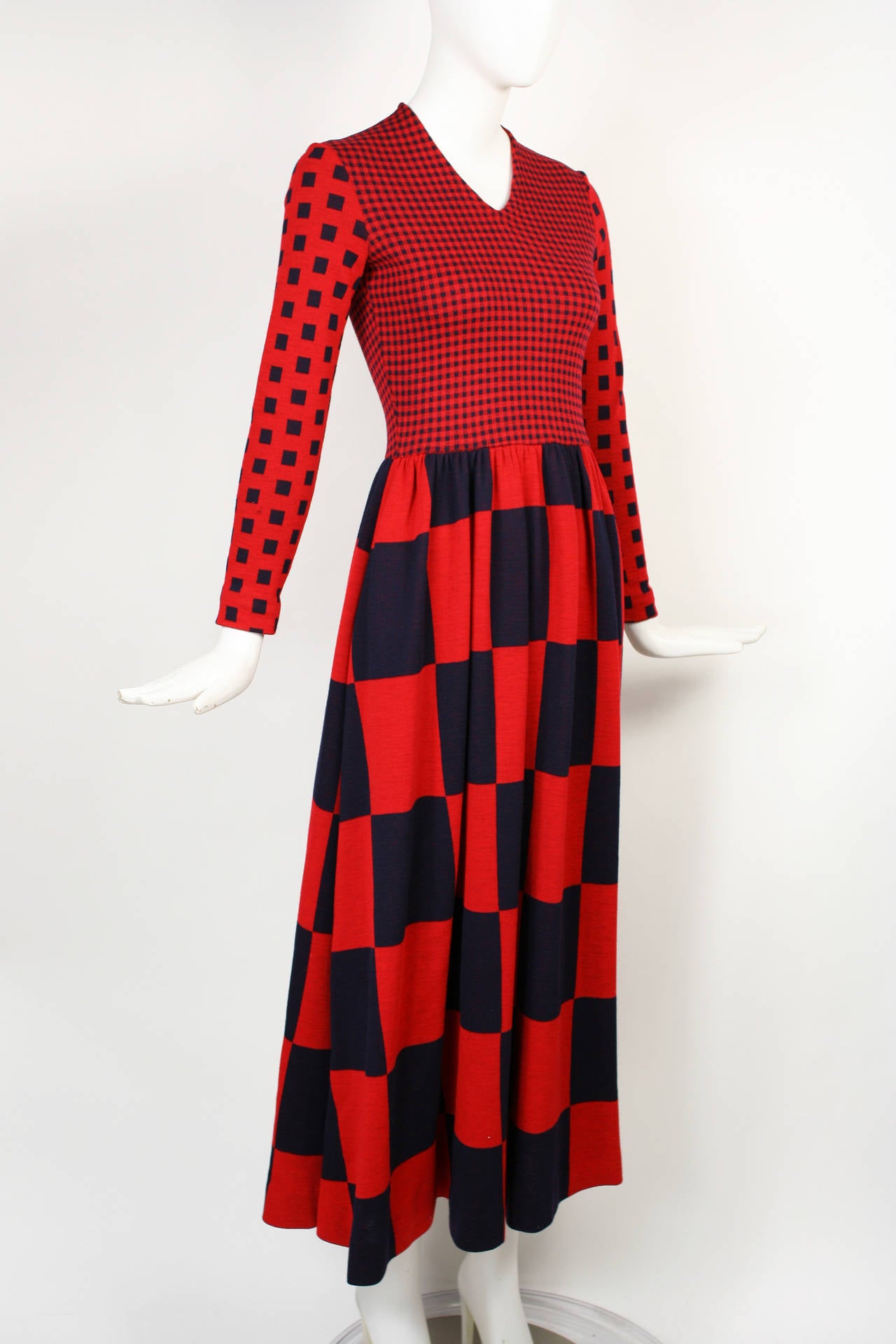 Iconic vintage 70s maxi dress from designer Rudi Gernreich. Made of stretch wool. Op-art check print of varying sizes in red and a deep dark blue that is almost black. Fitted bodice has high v-neck and long fitted sleeves. Full-length skirt is