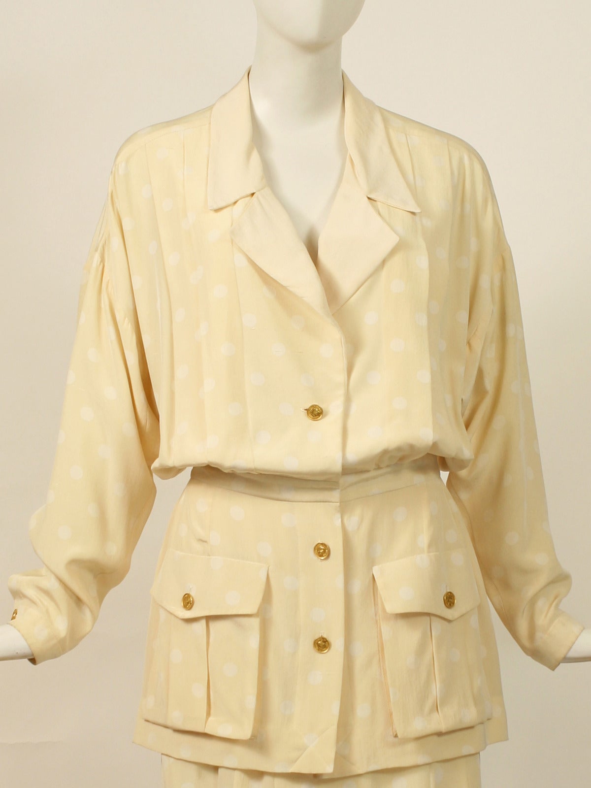 1990's Chanel Cream and White Polka-Dot Silk Suit
This a lovely suit made with polka dot silk fabric in a safari style silhouette . Pleated skirt. Gold Coco Chanel profile buttons throughout. Pleating detail on the back of  blouse. 
Excellent