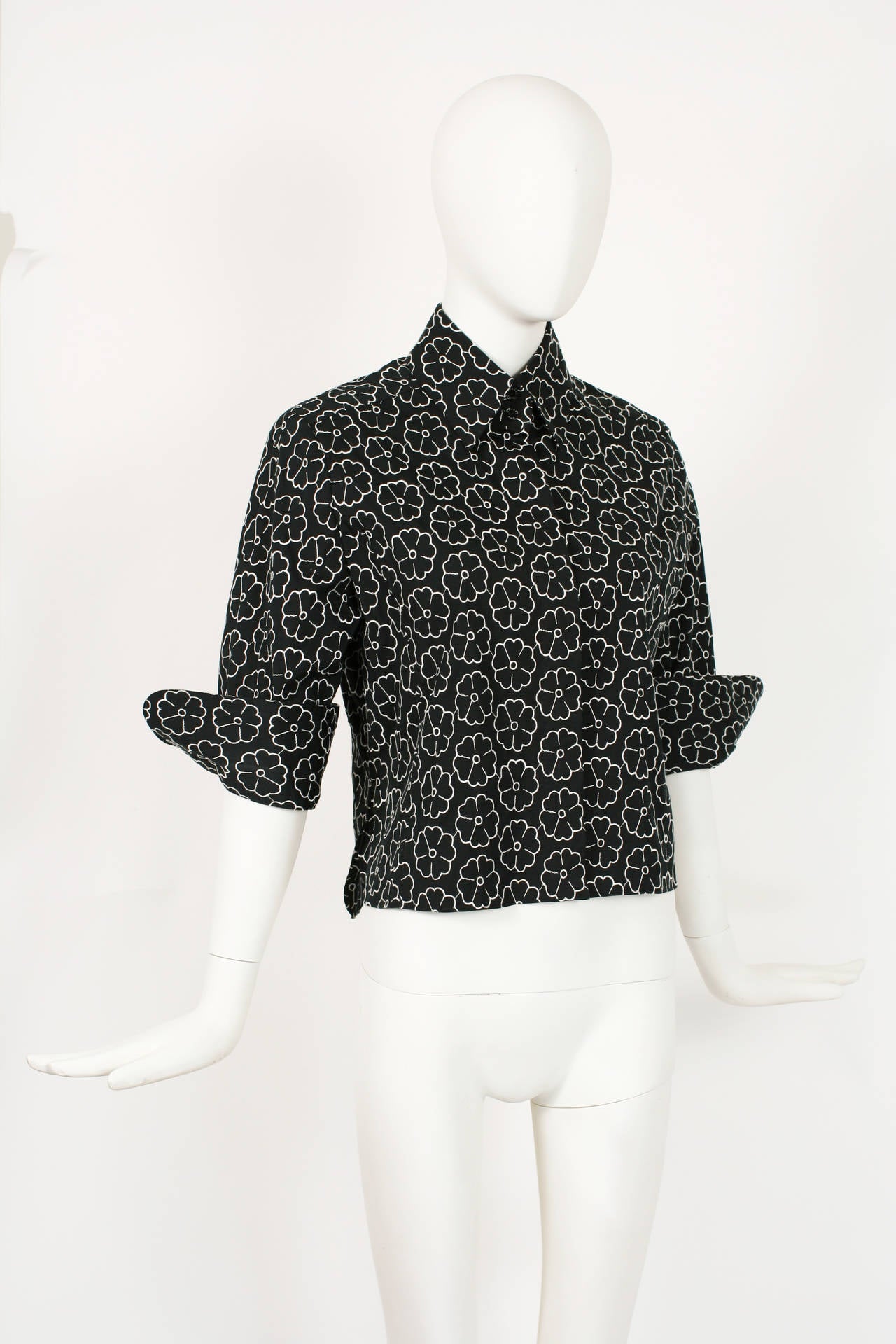 CHANEL black button down shirt embroidered with camellias, 3/4 length sleeves with side slits at bottom. Five  small buttons etched CHANEL PARIS.  
From the 2004 P collection. Size 44 or medium.  
The fabric is 78% cotton, 17% polyamide and 5%