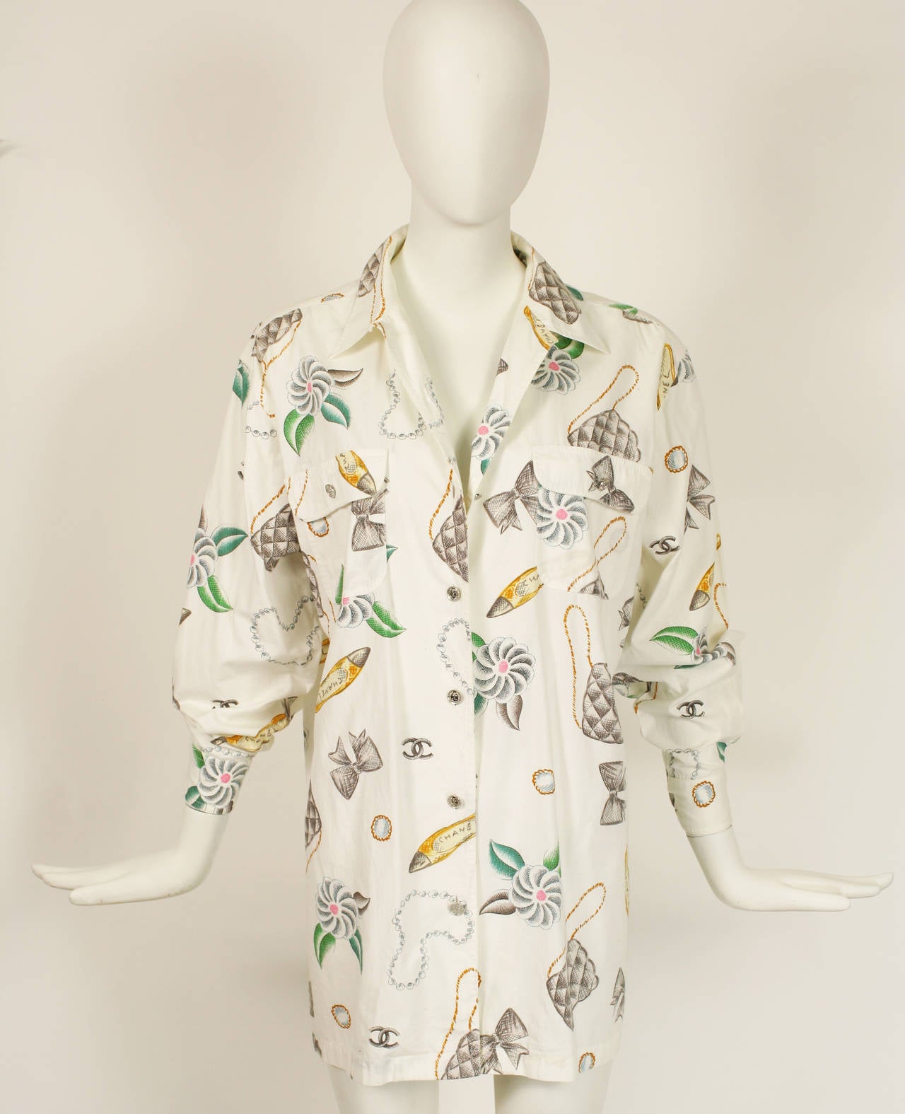 CHANEL button down shirt with camellias, logos, ballerinas, jewelry, bows, quilted bags. Oversized shirt that sound be belted and worn as a dress.  
Silver Chanel 31 Rue Cambon Paris buttons with two buttons on each cuff.  Cotton. Excellent