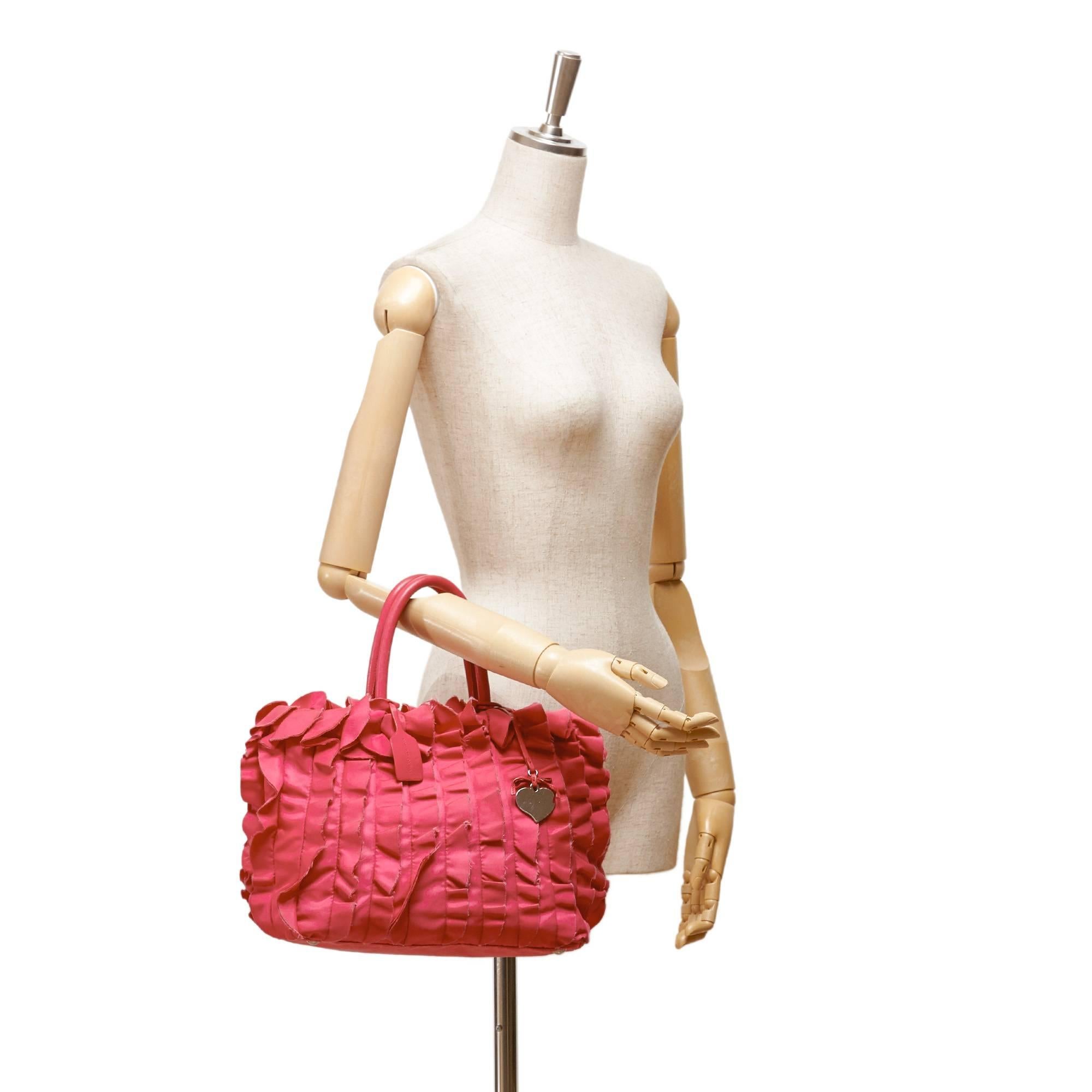 - Ce sac fourre-tout rose de Prada présente un corps en satin, des anses en cuir roulées, un dessus ouvert avec fermeture magnétique et une poche intérieure zippée. Le sac est agrémenté d'une breloque en forme de cœur en métal argenté. Girly, ruffle