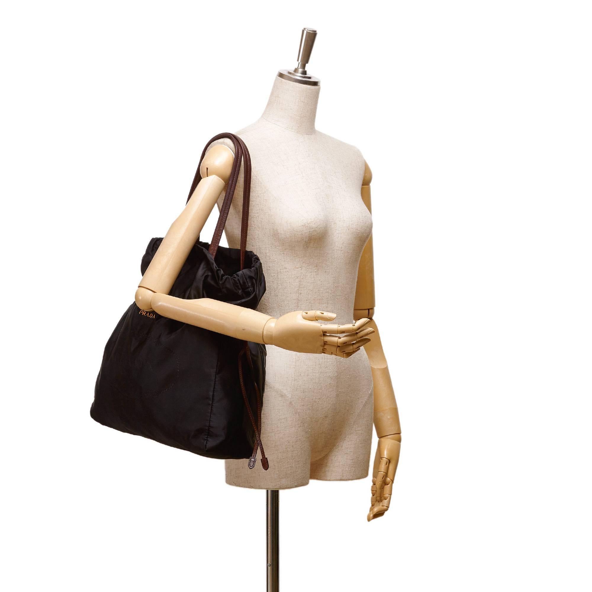- This Prada black tote bag features a nylon body, flat brown leather straps, drawstring closure, and interior zip pocket. A very chic and lightweight to carry tote bag for daily use. 

- Made in Italy. 

- Size: 37cm x 38.5cm x 11cm. Handle and
