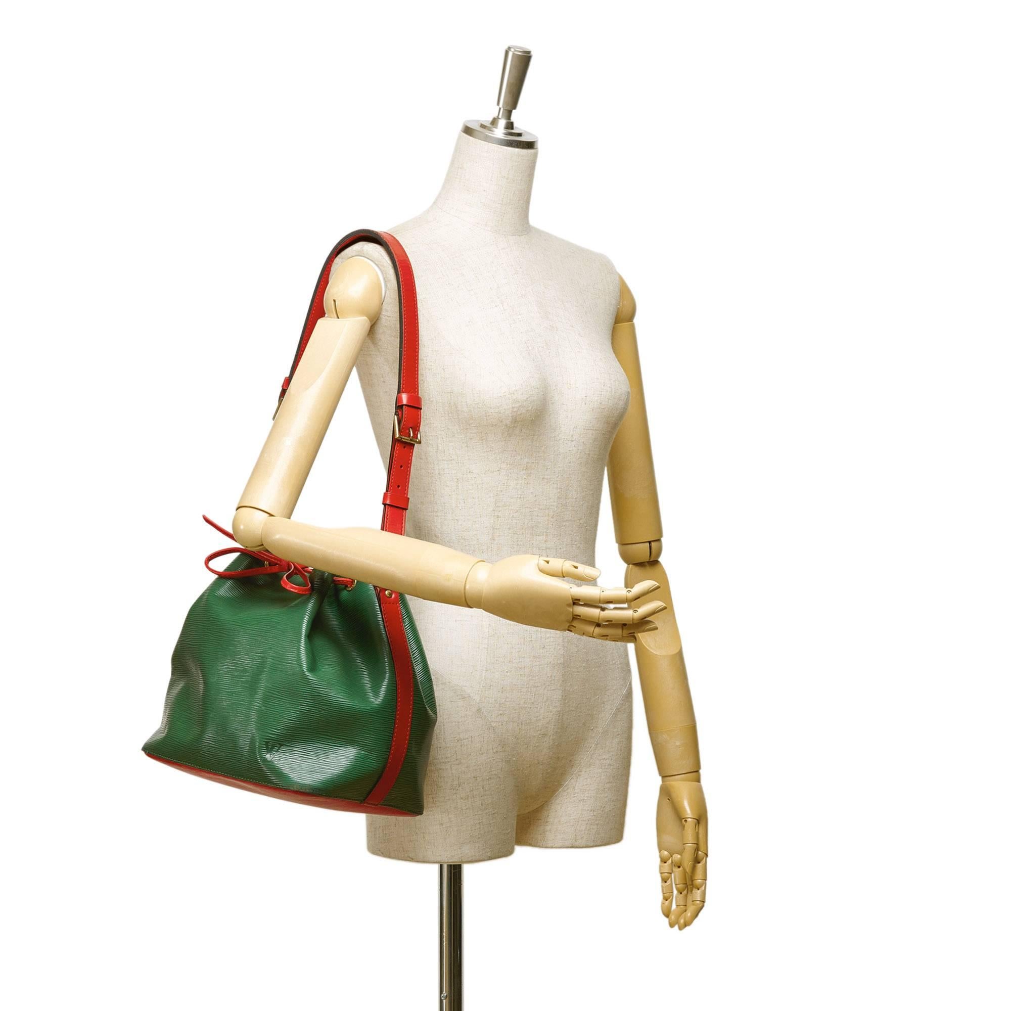 - This vintage 1994 Louis Vuitton petit noe features a green and red epi leather, an adjustable flat strap, an open top with a drawstring closure, and Alcantara lining. Rare and interesting colour combination Louis Vuitton shoulder bag!

- Made in