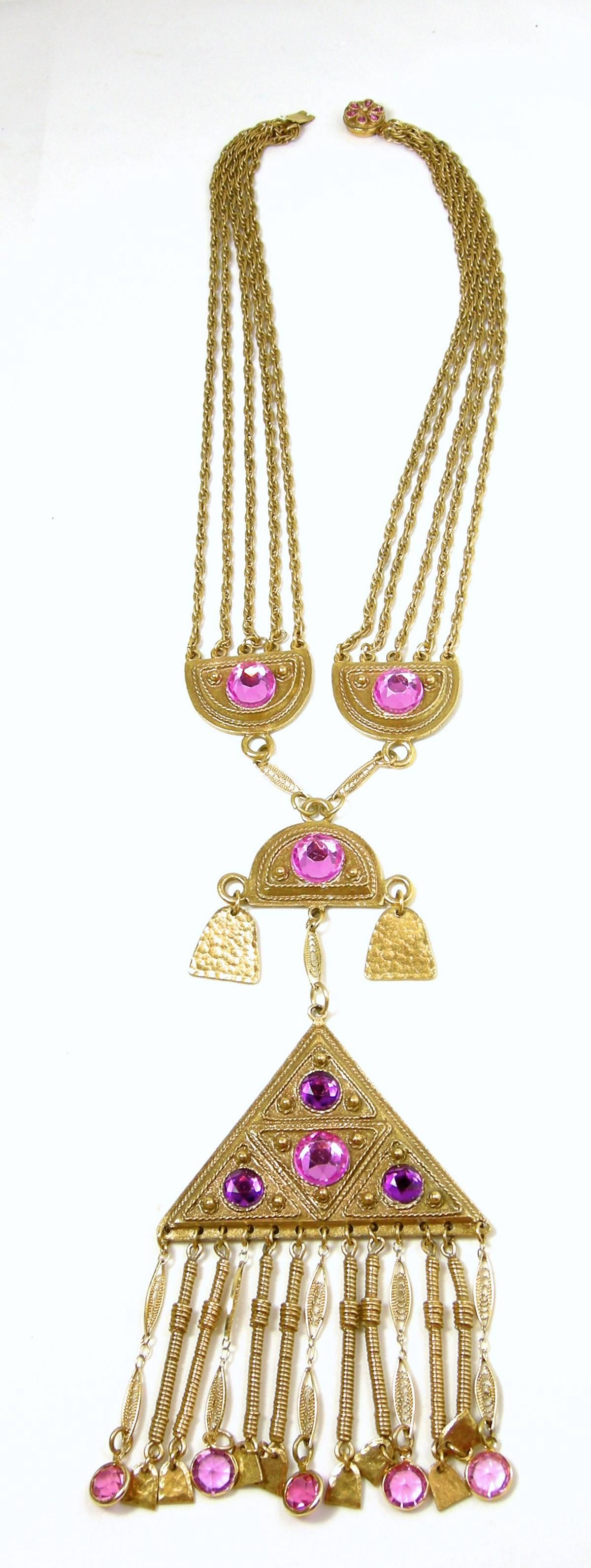 This is an extraordinarily large vintage Vendome necklace from the1960s. It features a triangular shaped centerpiece that has fringes with purple and pink round faceted crystals. It has 3 half-moon shaped vintage gold tone metal pieces on top