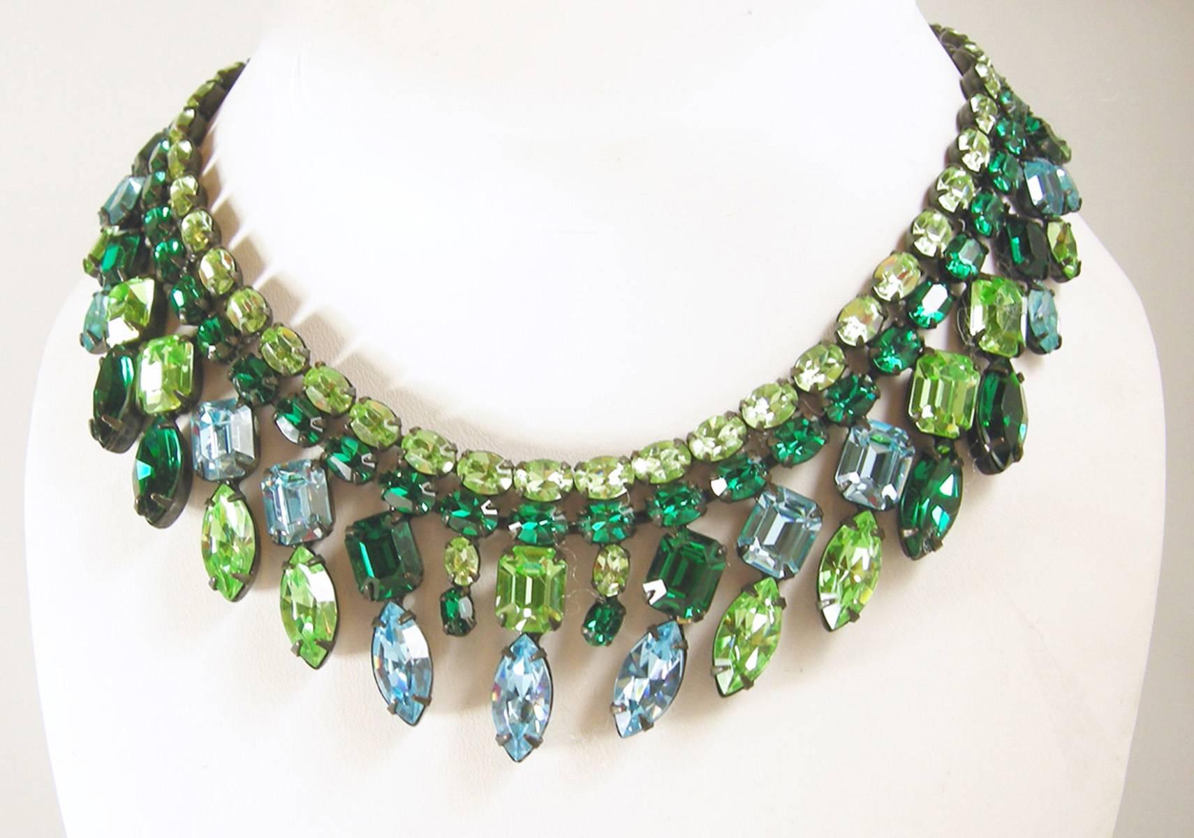 This vintage signed1950s Schreiner necklace has the inverted crystals that Schreiner is famous for. It combines different shapes and shades of green crystals creating a breathtaking collar necklace. The necklace is 14” x 1-1/2”. It has Japanned