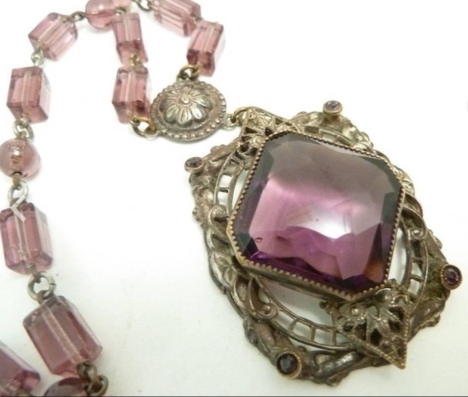 This vintage deco Czech piece features amethyst color glass in a gold-tone setting.  In excellent condition, the pendant measures 1 7/8” x 1 ½” 