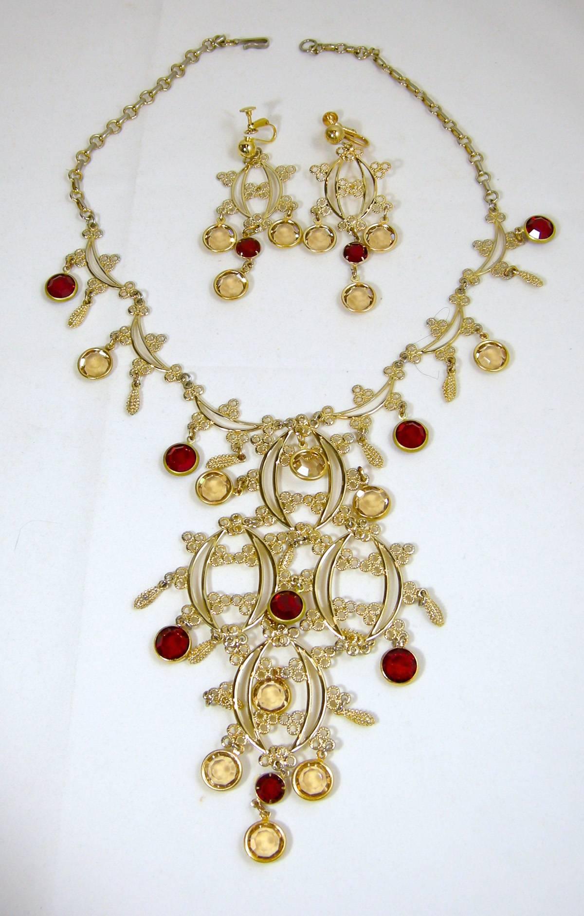 This huge1960s Hobe crystal bib necklace set has faux ruby and citrine crystals dangling from it with an open work design. In a gold tone setting, it measures 17” x 1/4”. The bib measures 5” x 3”.  It has a hook closure. The matching clip earrings