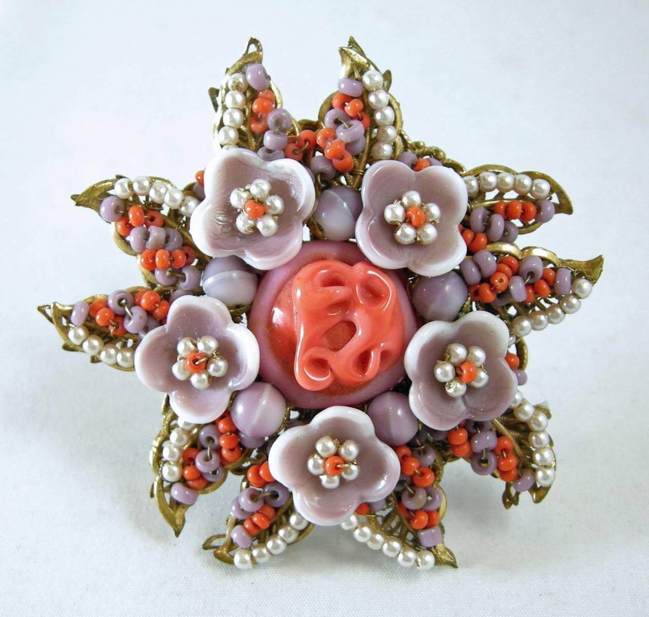 This vintage 1940s signed Miriam Haskell brooch pin features an ornate floral design with coral, lavender glass beads and seed faux pearls in a gold-tone setting.  In excellent condition, this pin measures 2-1/2” in diameter with a c-pin clasp and
