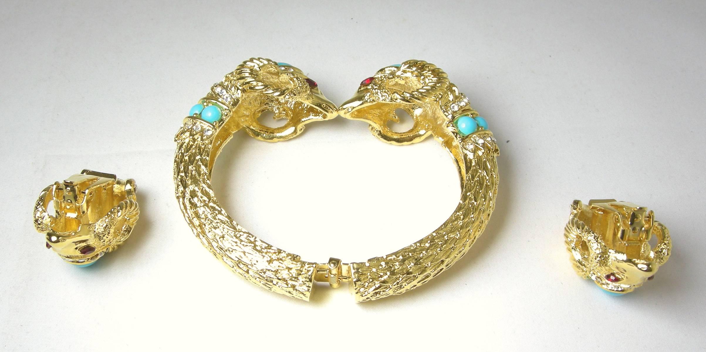 This Kenneth Jay Lane Ram bracelet is adorned with faux turquoise and clear colored crystals.  It has ruby colored crystals for eyes. The bracelet is set in a brilliant gold tone setting and has an etched snake like pattern. It measures 8” x 1-1/4”