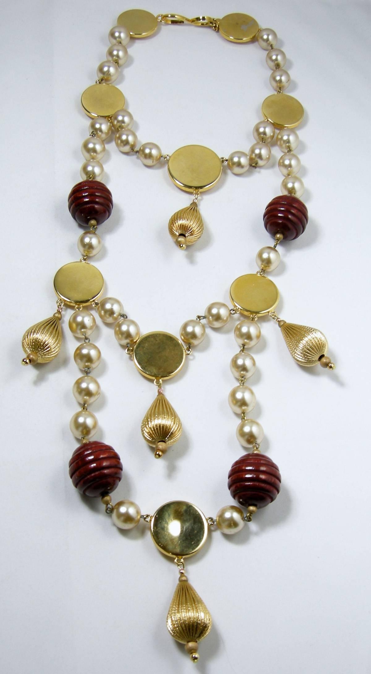 This vintage Roger Scemama necklace done for Yves St. Laurent (YSL) features a multi-strand design with large, ridged dark wood and gold-tone balls with faux pearl accents in a gold-tone setting.  In excellent condition, this necklace measures 16
