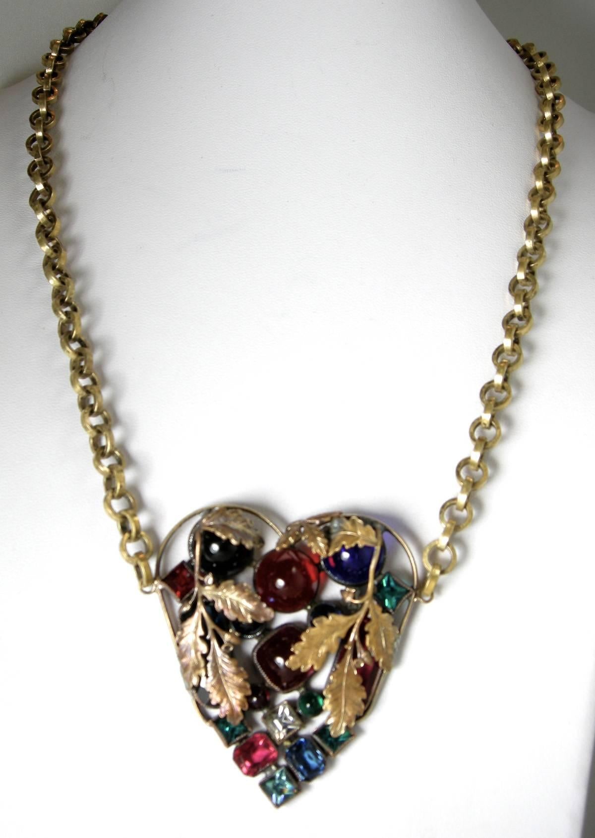 This is a gorgeous Czech heart necklace from the 30s.  It has green, red, blue rhinestone accented with gold-tone leaves overlapping the stones. The chain is 23” long.  The heart measures 2-1/2” x 2-1/4” and has a spring back clasp.  This necklace