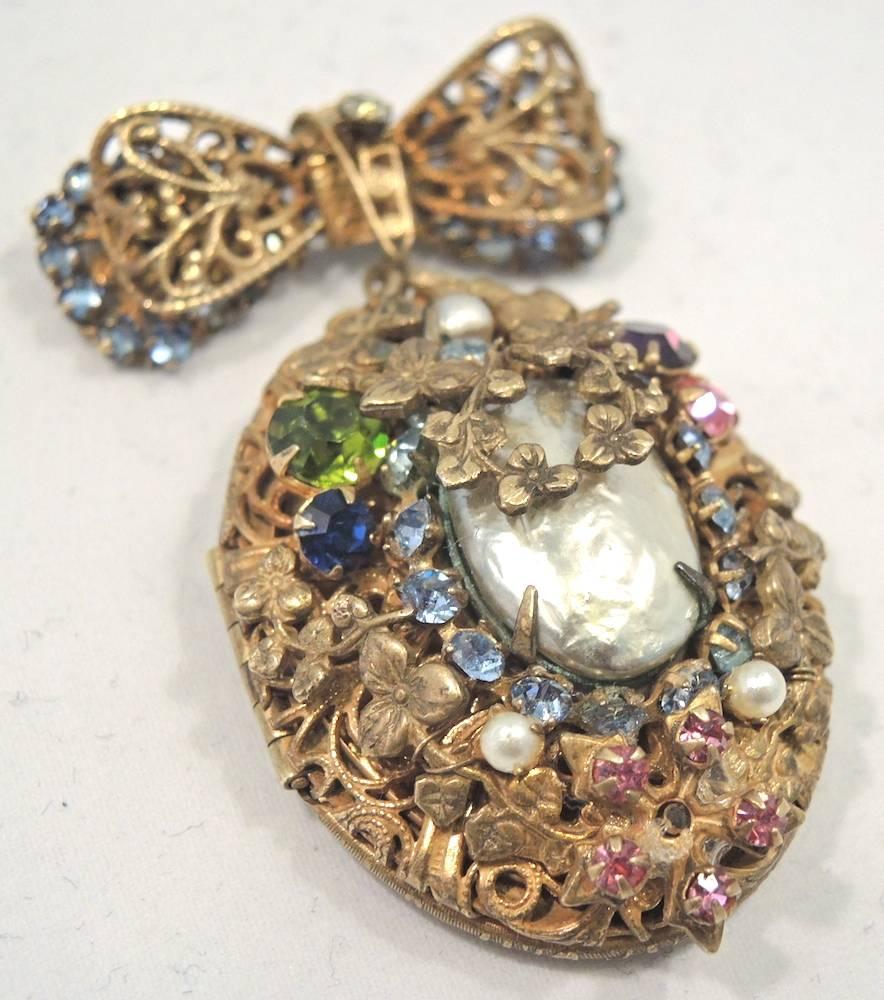 I have not seen this design in a long time.  This stunning signed Miriam Haskell brooch is designed with a bow top, which the locket hangs from.  The locket has an intricate design with multi colored crystals with a large baroque faux pearl in the