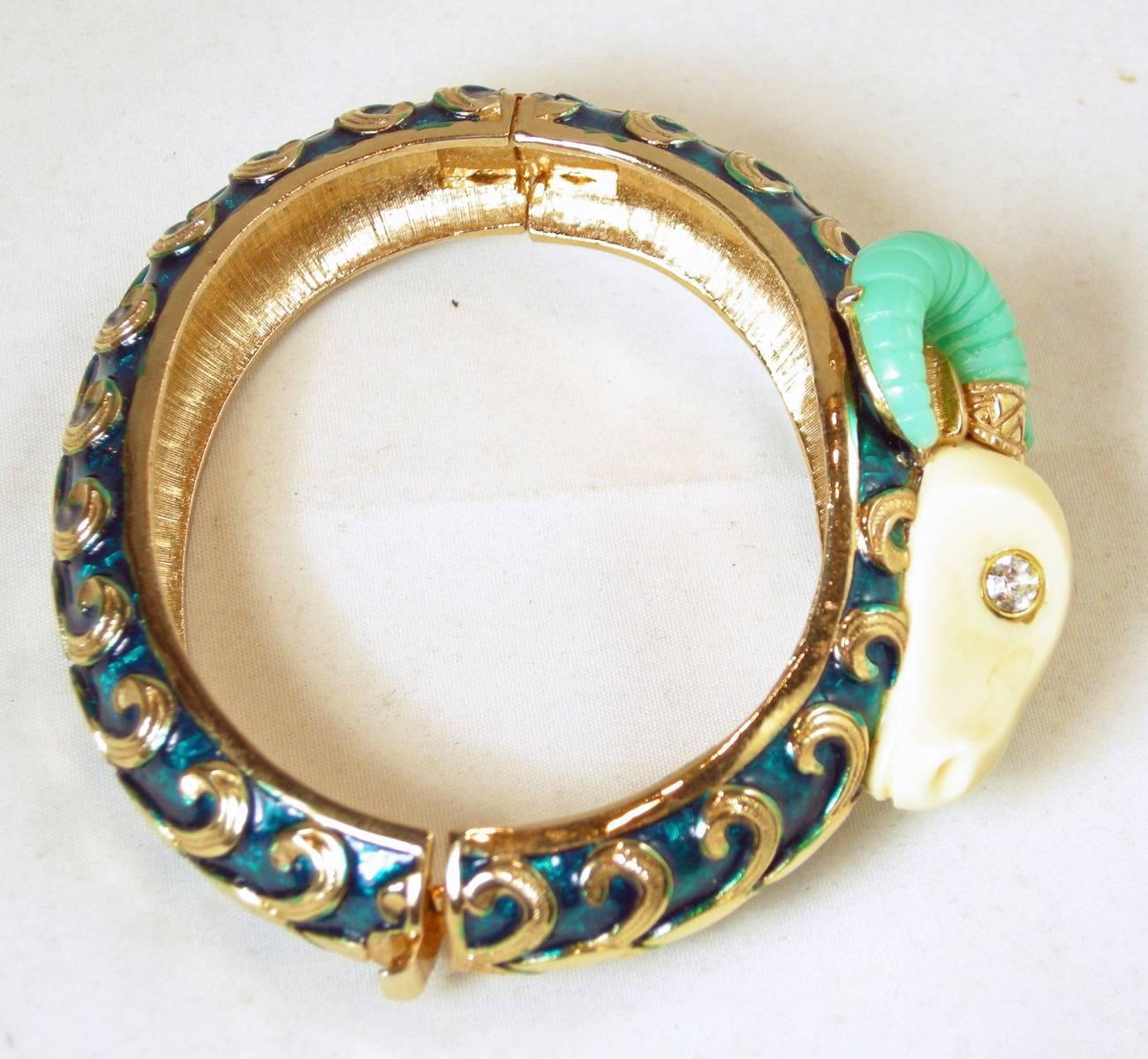 This rare vintage bracelet is made with green enamel and has a gold tone swirl design. The head of the ram has faux ivory and turquoise horns with crystal eyes. The bracelet is set in a gold tone setting and measures 9” x 1-1/2” at its widest part.