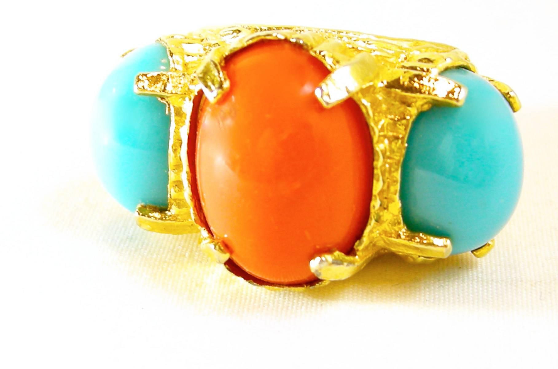 This vintage 1980s cocktail ring has faux coral and turquoise cabochon stones. It is set in a gold tone setting with a weave design. The top measures 2” across and 1” wide. The ring is a size 8, unsigned and in excellent condition.