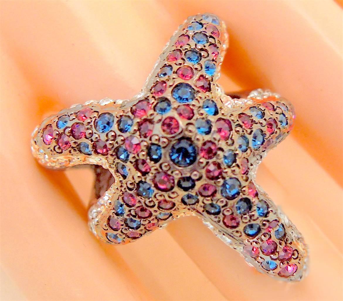 This Kenneth Jay Lane ring reminds me of a beautiful summer day!  It has pink, blue and clear crystals in a pewter metal setting and measures 1-1/2” x 1” and is adjustable up to a size 8.  It is signed “Kenneth Lane” and is in excellent condition.  