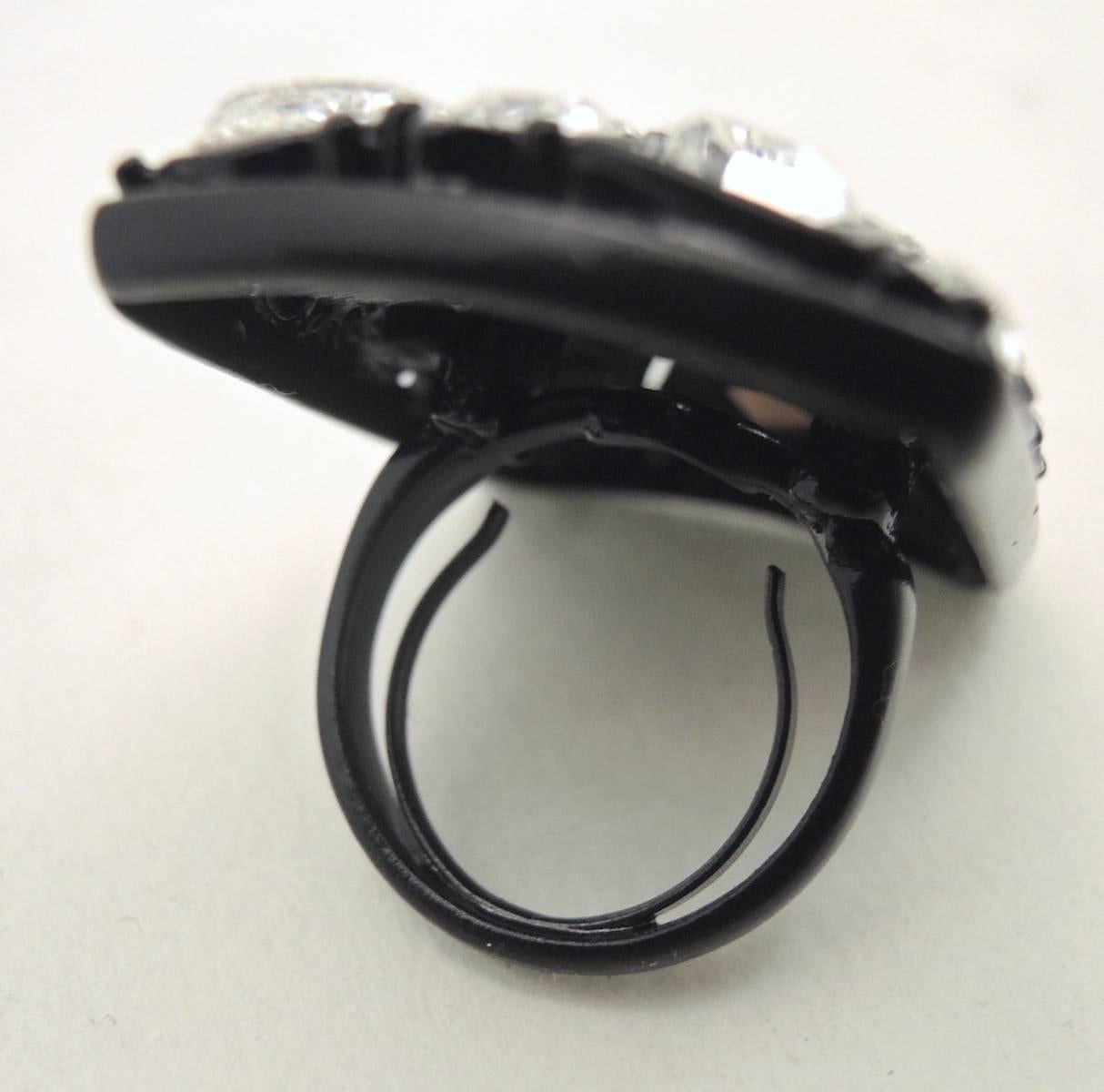 This is a dramatic and large sized rectangle crystal ring. The crystals are made in different shapes on black enameling over metal. It measures 1-1/2” x 1-1/4”. The ring is adjustable up to a size 7 and signed “Kenneth Lane”.  It is in excellent
