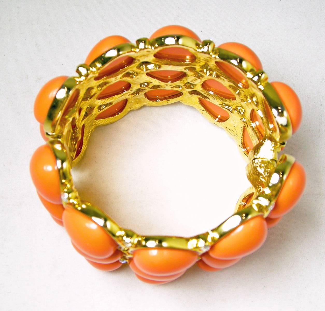 This is a magnetic clamper bracelet made by Kenneth Jay Lane. It is made with segmented chunky faux coral color cabochon stones set in a bright gold tone setting. It measures 7” x 2” and is signed “KJL”.  It is in excellent condition.
