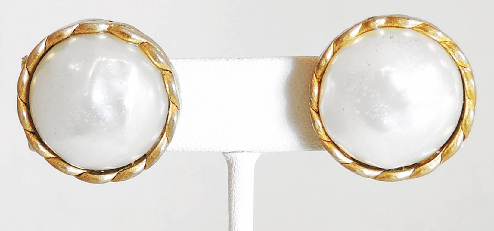 These vintage Chanel faux pearl clip-on earrings date back from 1984. The design has a large Chanel glass faux pearl in the center with a twisted rope design frame. They measure 1” x 1”. They are signed “Chanel” with the double “CC 1984”. They are