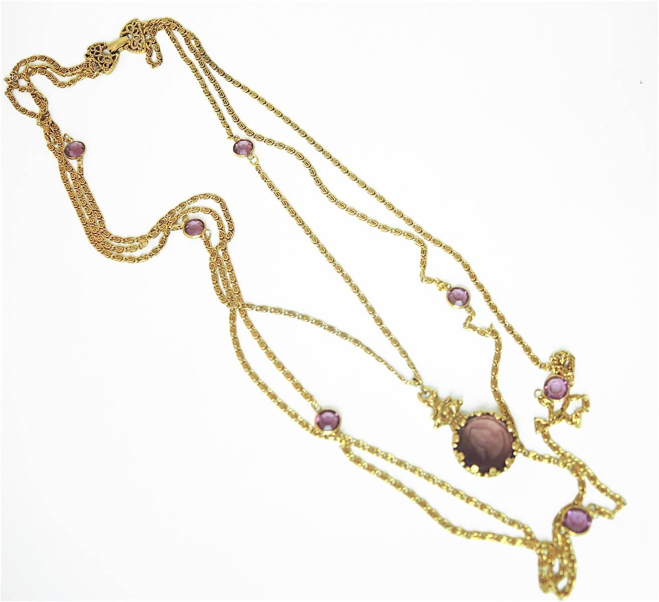 This vintage 1960s Goldette necklace features one chain with a faux amethyst cameo pendant and two more chains with amethyst color discs in a gold-tone setting. The first chain with the cameo measures 24”, the second chain is 30” and the third is