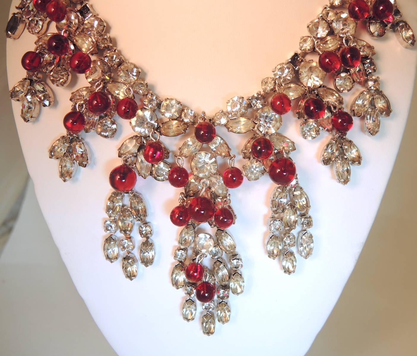 This stunning necklace by Kramer features red poured glass cabochons with cascading cluster of clear crystals in a silver-tone setting.  This piece measures 16” x 3-1/2” at the widest part.  It is signed “Kramer” and is in excellent condition.  