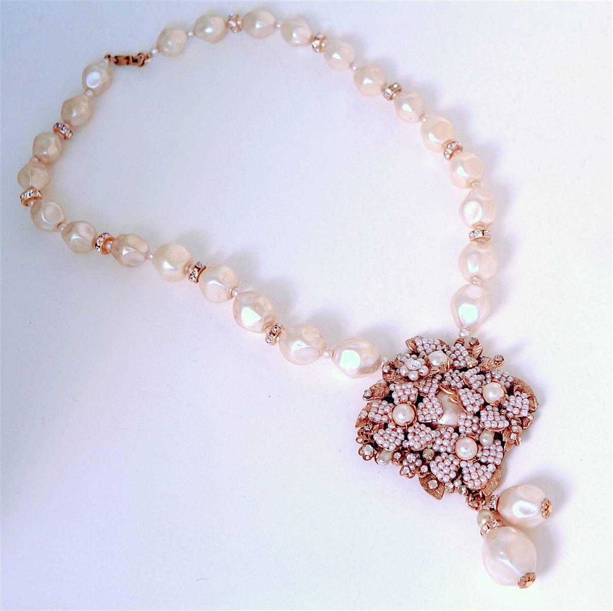 This classic Miriam Haskell necklace features an ornately designed centerpiece of faux seed pearls and rose montee accents in a gold-tone setting. The necklace also has crystal rondelle spacers in between the large faux pearls. The necklace measures