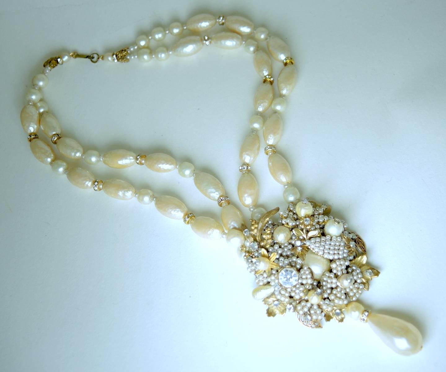 This striking Miriam Haskell necklace features an ornate centerpiece with seed pearls and rose montee accents in a gold-tone setting. There is a large oval teardrop pearl that dangles at the bottom of the centerpiece. The double strands are made