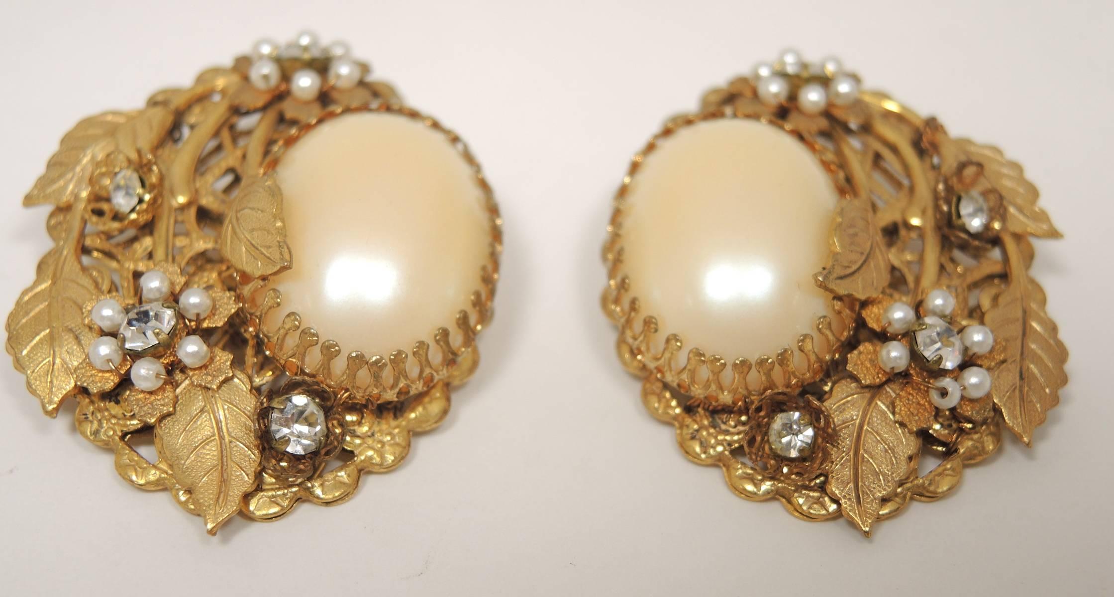 These vintage earrings resemble Miriam Haskell's design with a large faux pearl center and clear rhinestone accents in a heavily etched floral style gold-tone setting. There earrings measure 1-3/8” x 1-1/4” and are in excellent condition.