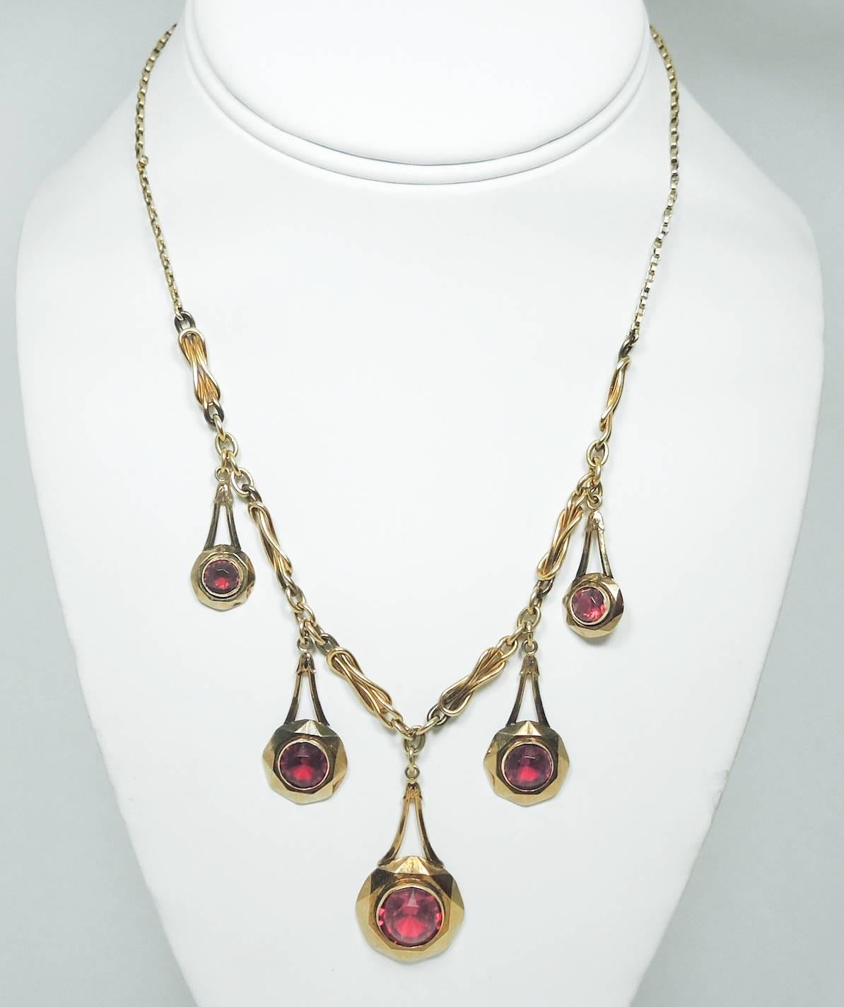 This vintage features five teardrop shaped drops with red rhinestone accents in a gold-tone setting. The necklace has a delicate link necklace with a spring ring clasp. It measures 16” x 1/8” with the longest center drop measuring 1-1/2” and is in