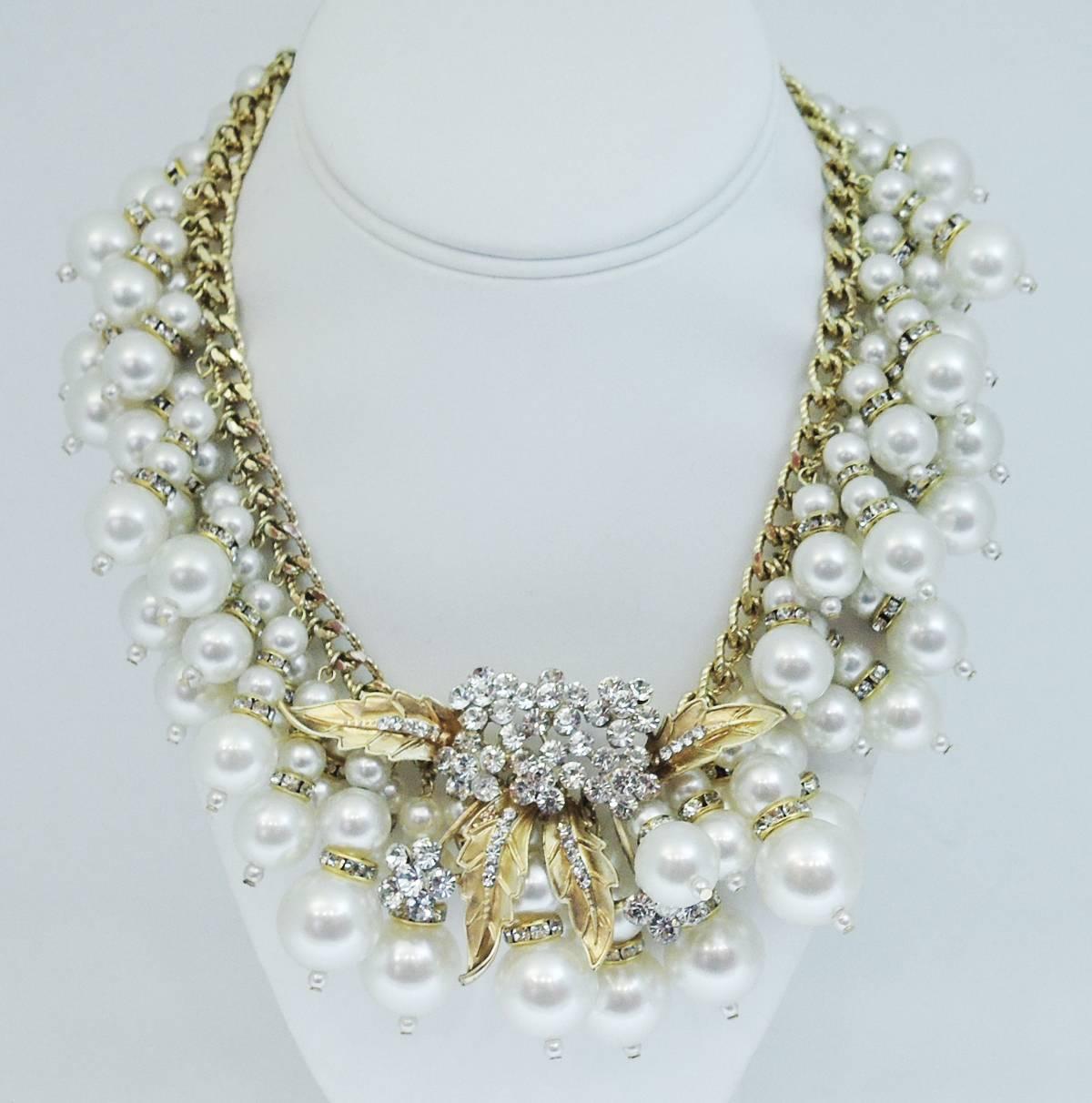 This one-of-a-kind Anka necklace features a massive amount of cascading faux pearls that dangle from a braided link necklace. The pearls have rhondelle spacers in between them and the detailed centerpiece has a floral leaf design with large round