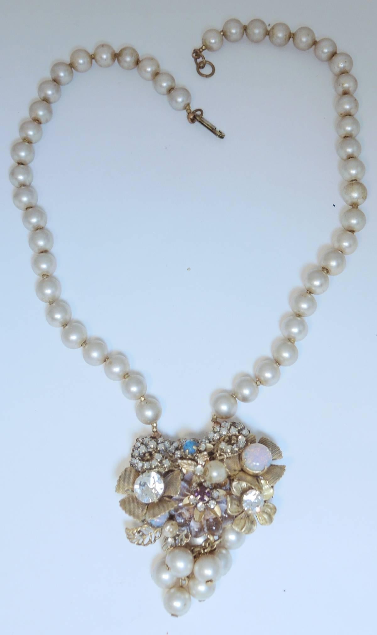 This vintage Miriam Haskell necklace features a single strand of faux pearls that lead down to a magnificent centerpiece. The centerpiece has golden leaves with a crystal and faux opal centers. The centerpiece is accentuated with rose montee stones.
